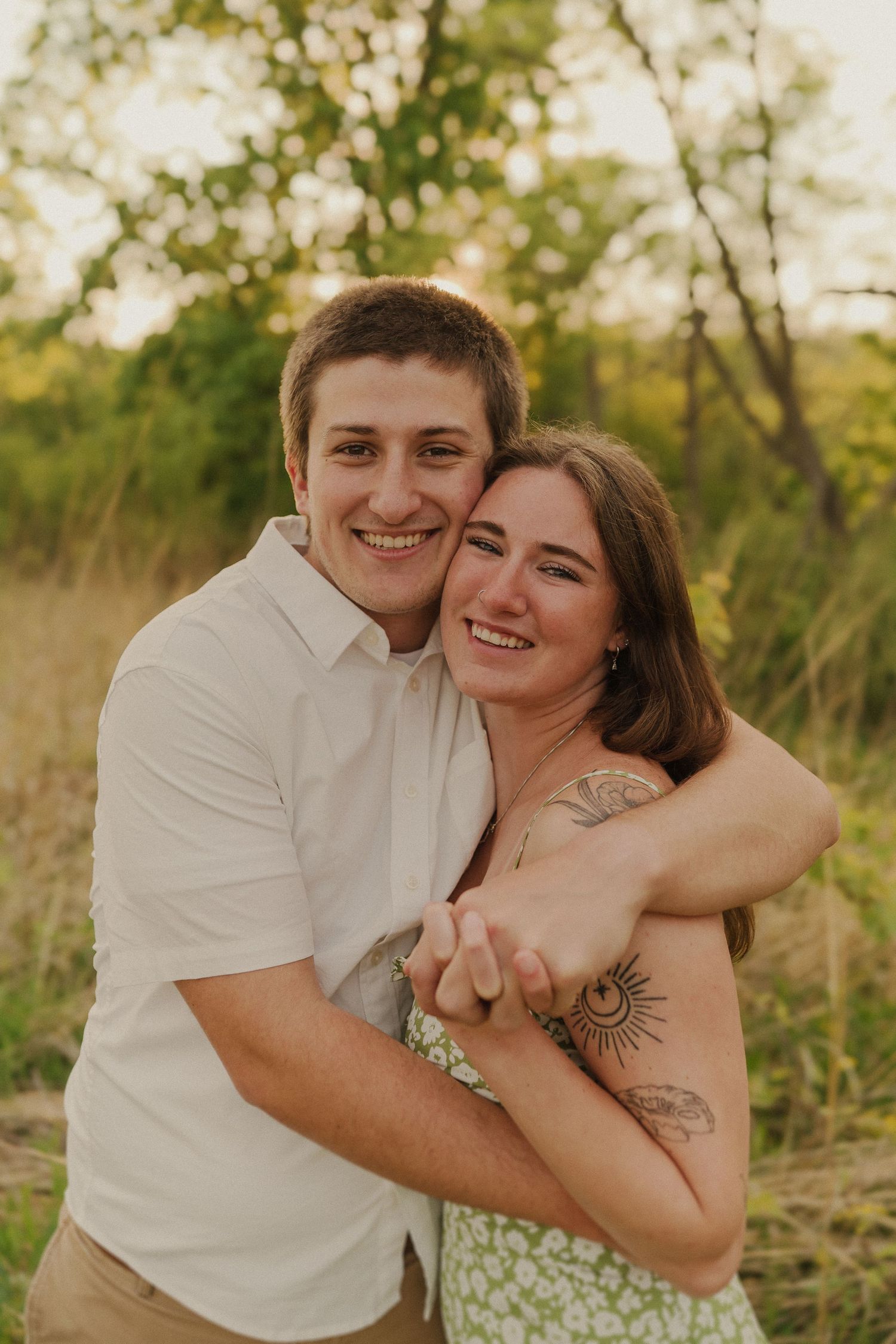 A cheerful couple shares a loving embrace while posing in a sun-drenched field at golden hour.