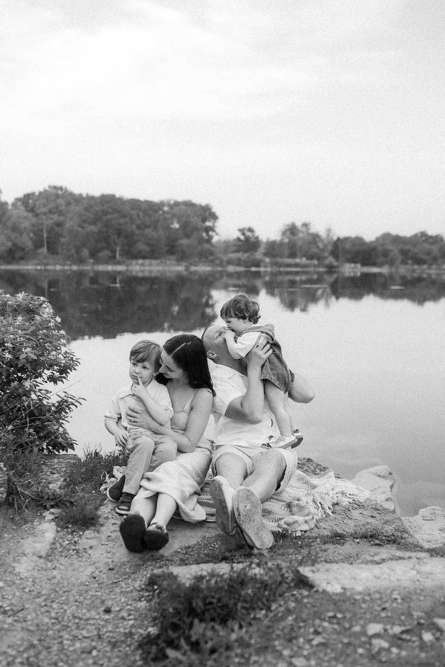 A black and white photograph showing a family relaxing together by a serene lake.