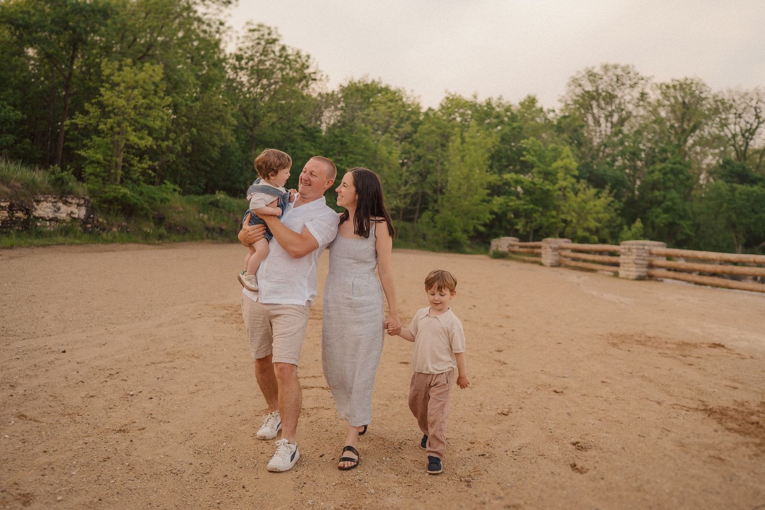 A family takes a sunset stroll together on a sand-covered path surrounded by trees.