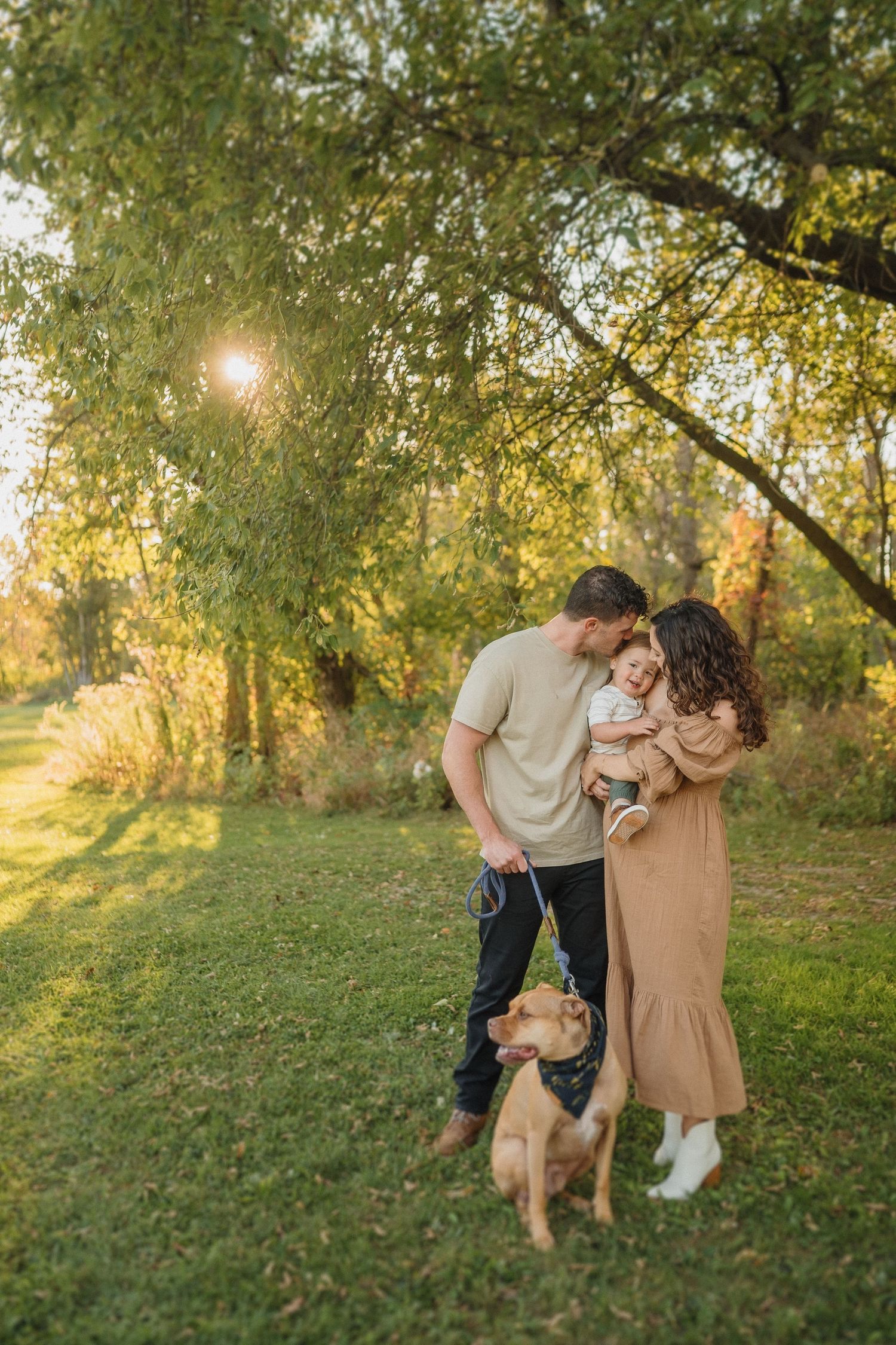 Intimate family moment in sun-dappled forest with their loyal dog beside them.