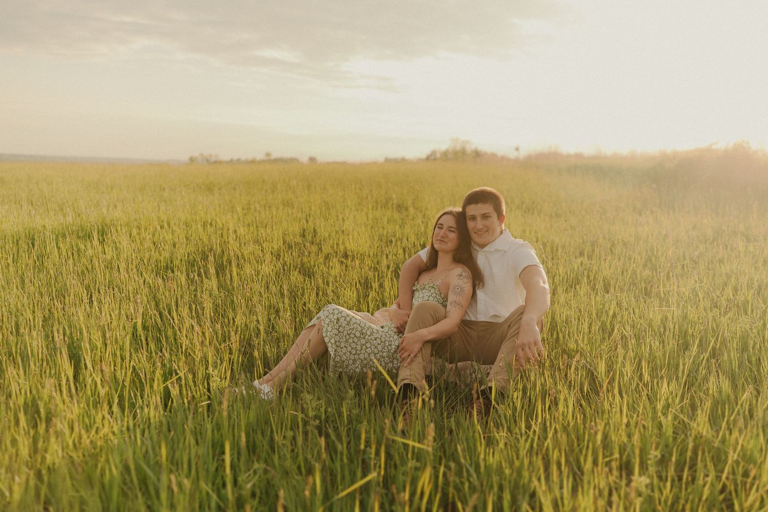 A couple sits together in a sunlit meadow during golden hour.