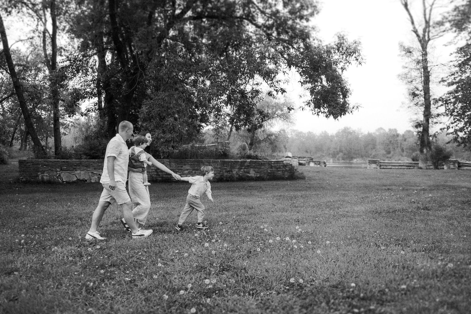 A playful black and white photograph captures movement as three people hold hands in a line on a grassy field.
