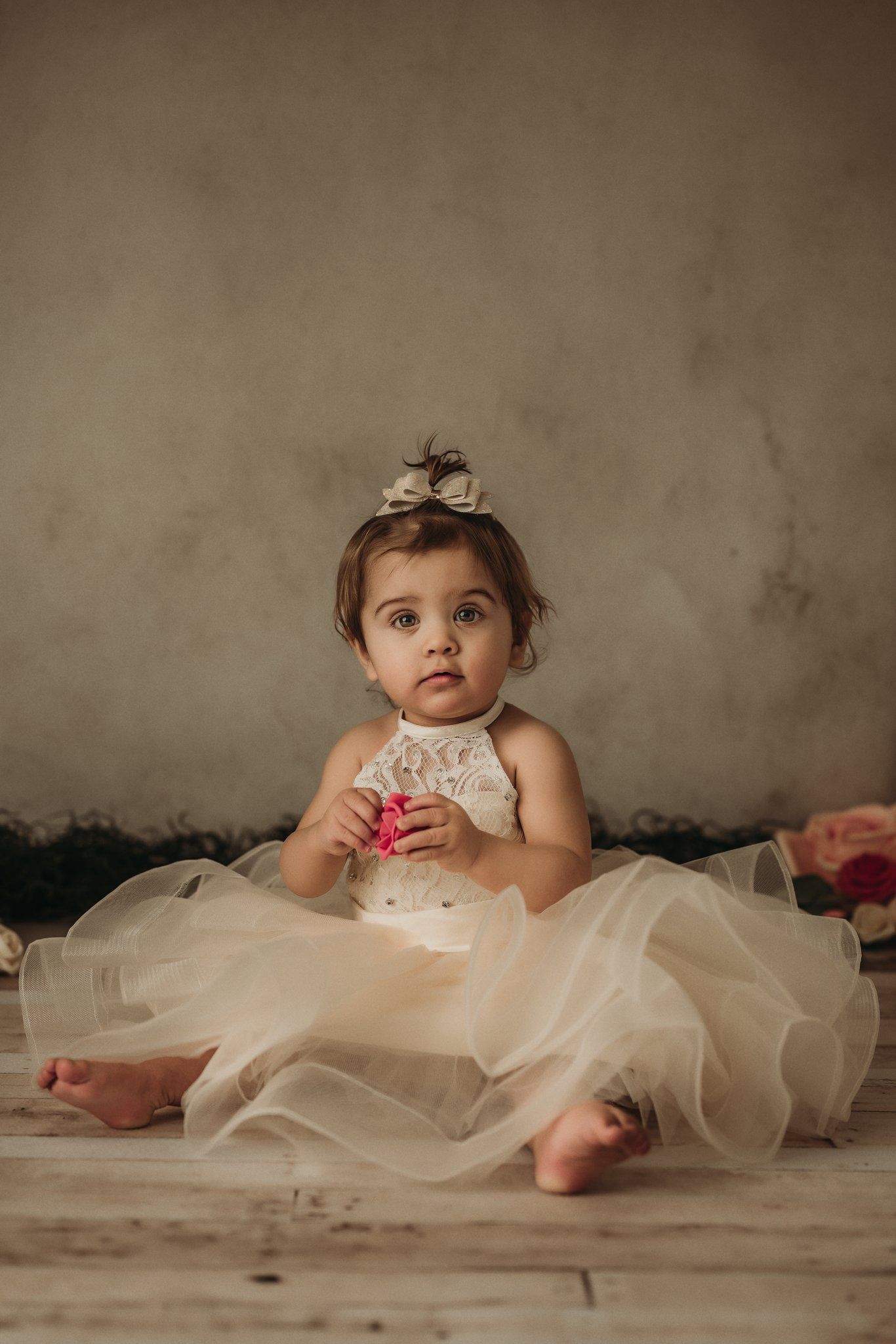 A dreamy portrait features a cream lace dress and floral hairpiece against a neutral backdrop.
