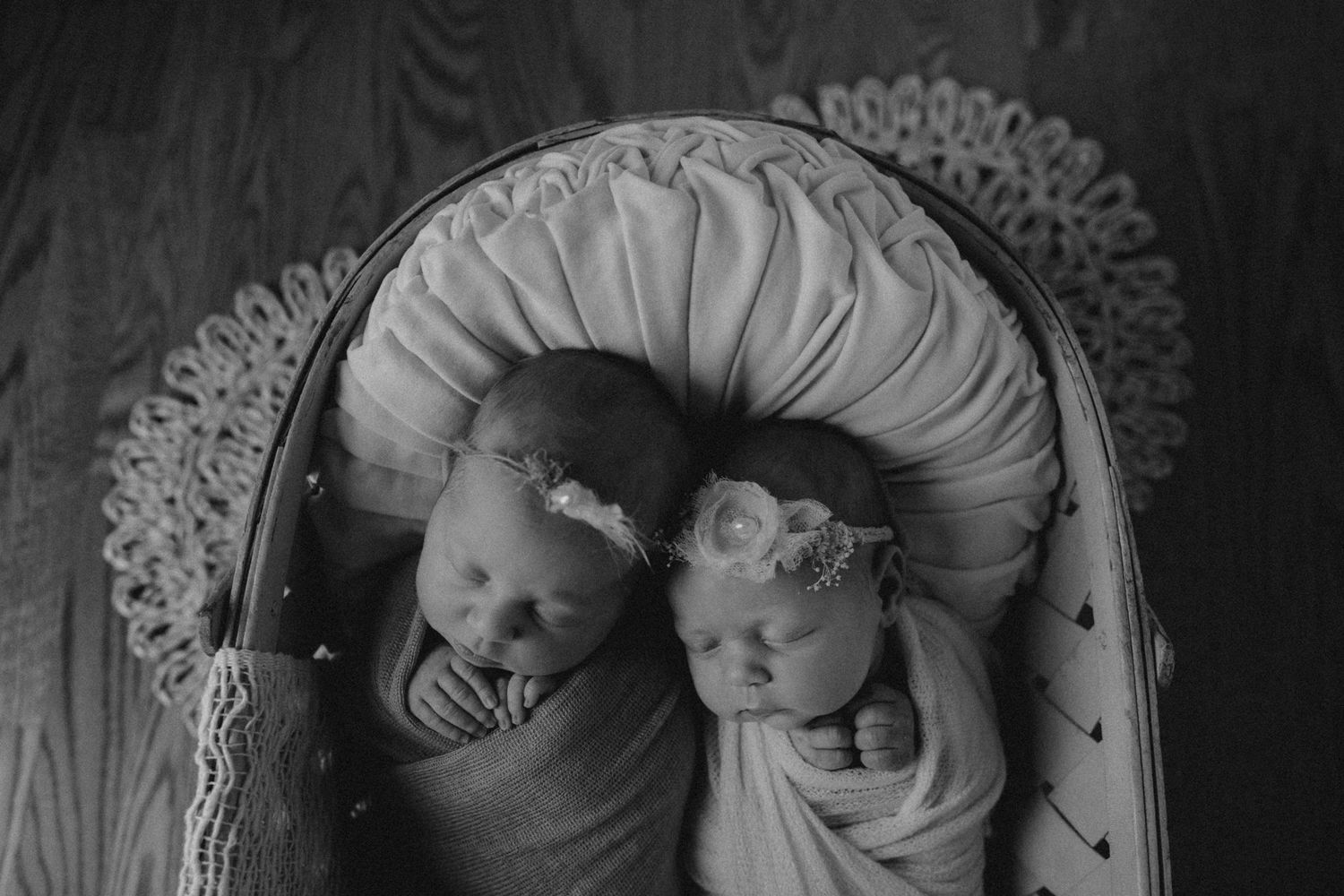 Two swaddled infants lying together in a vintage-style cushioned bassinet.