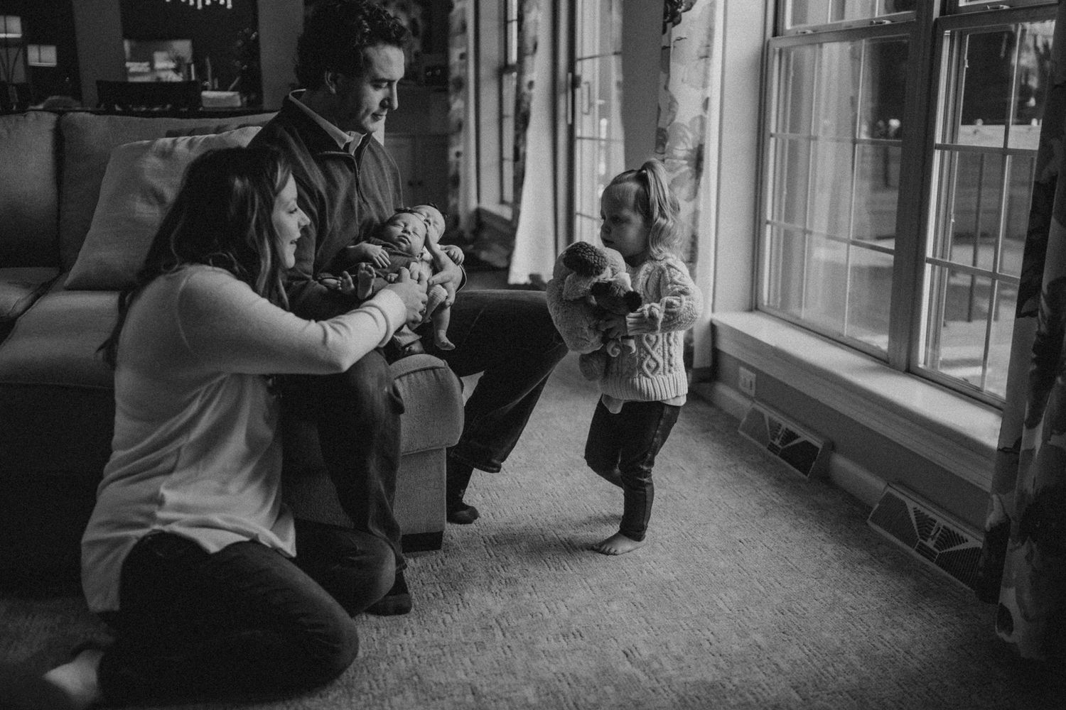 Black and white photo of family playing together in living room near window.