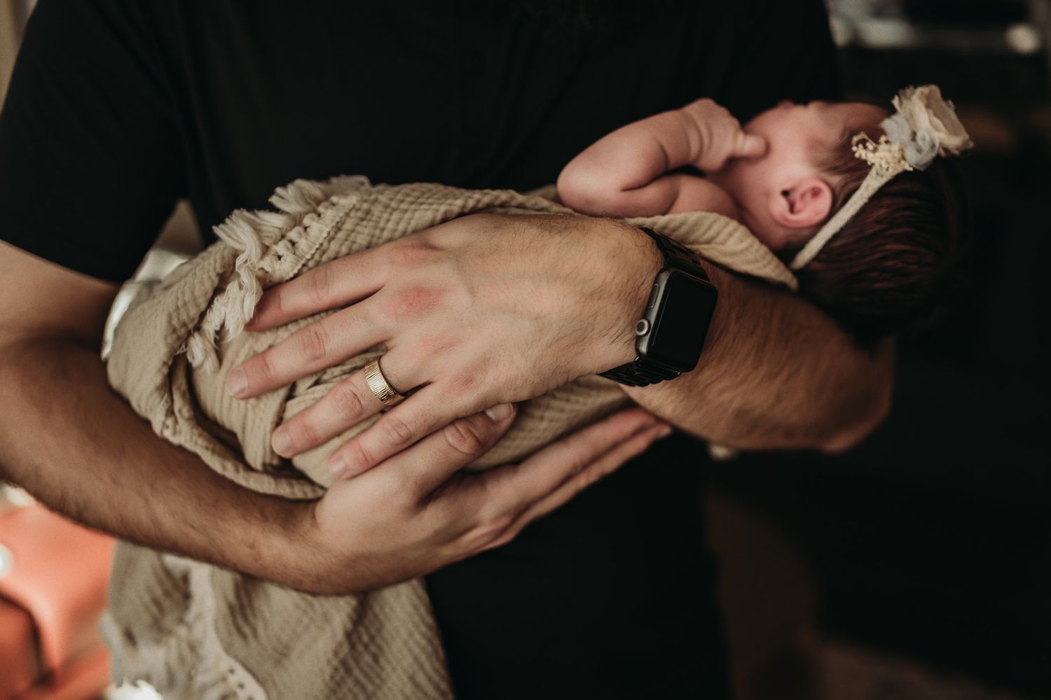A parent cradles their sleeping newborn wrapped in a beige knit blanket.