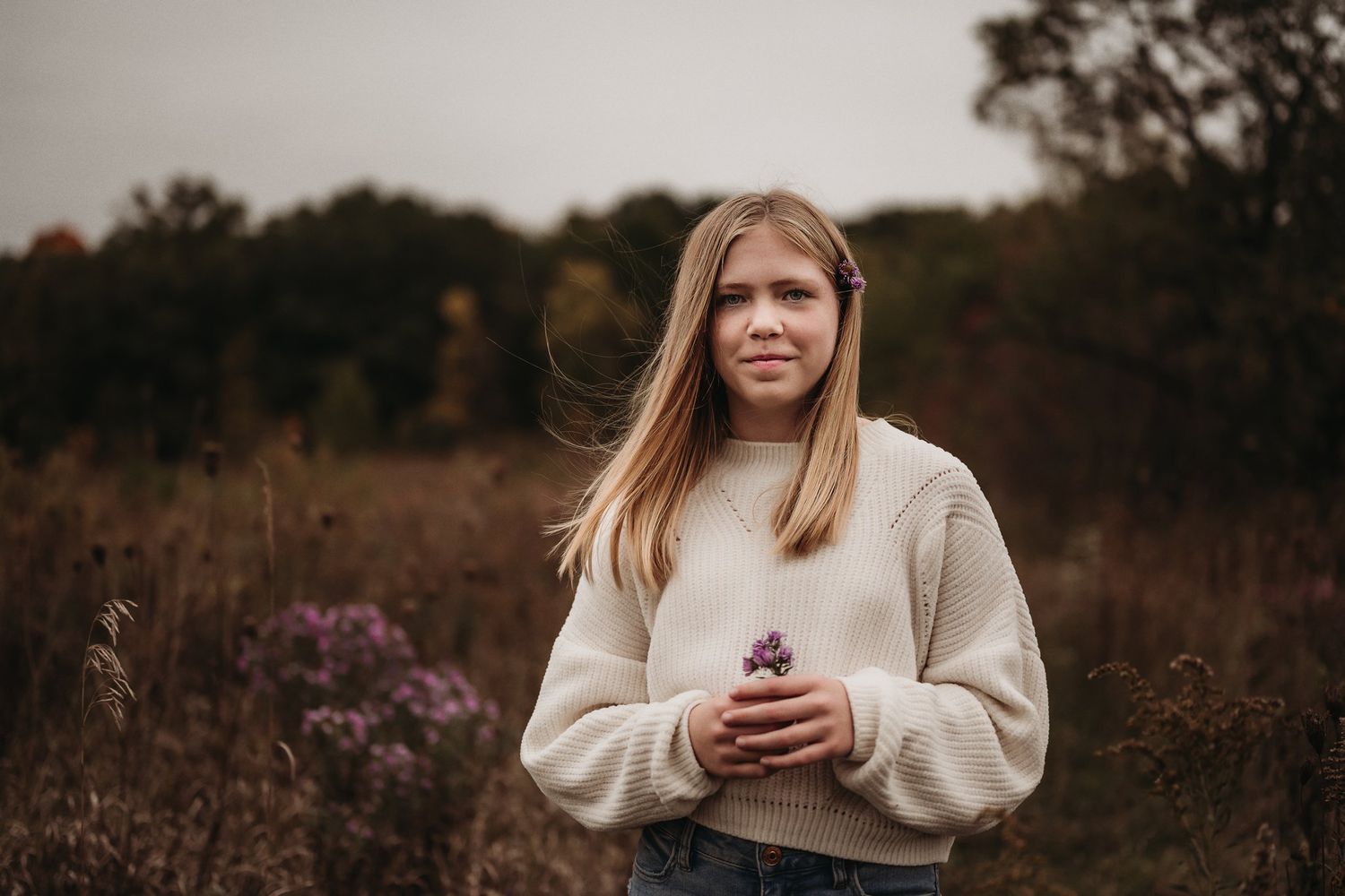 Person in a cream sweater standing in a fall meadow with purple wildflowers.