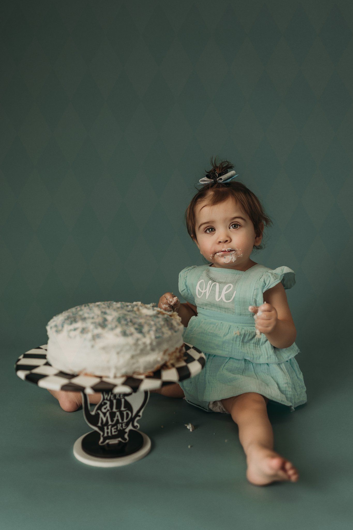 A celebratory cake smash session featuring a mint dress and decorative cake stand against a green background.