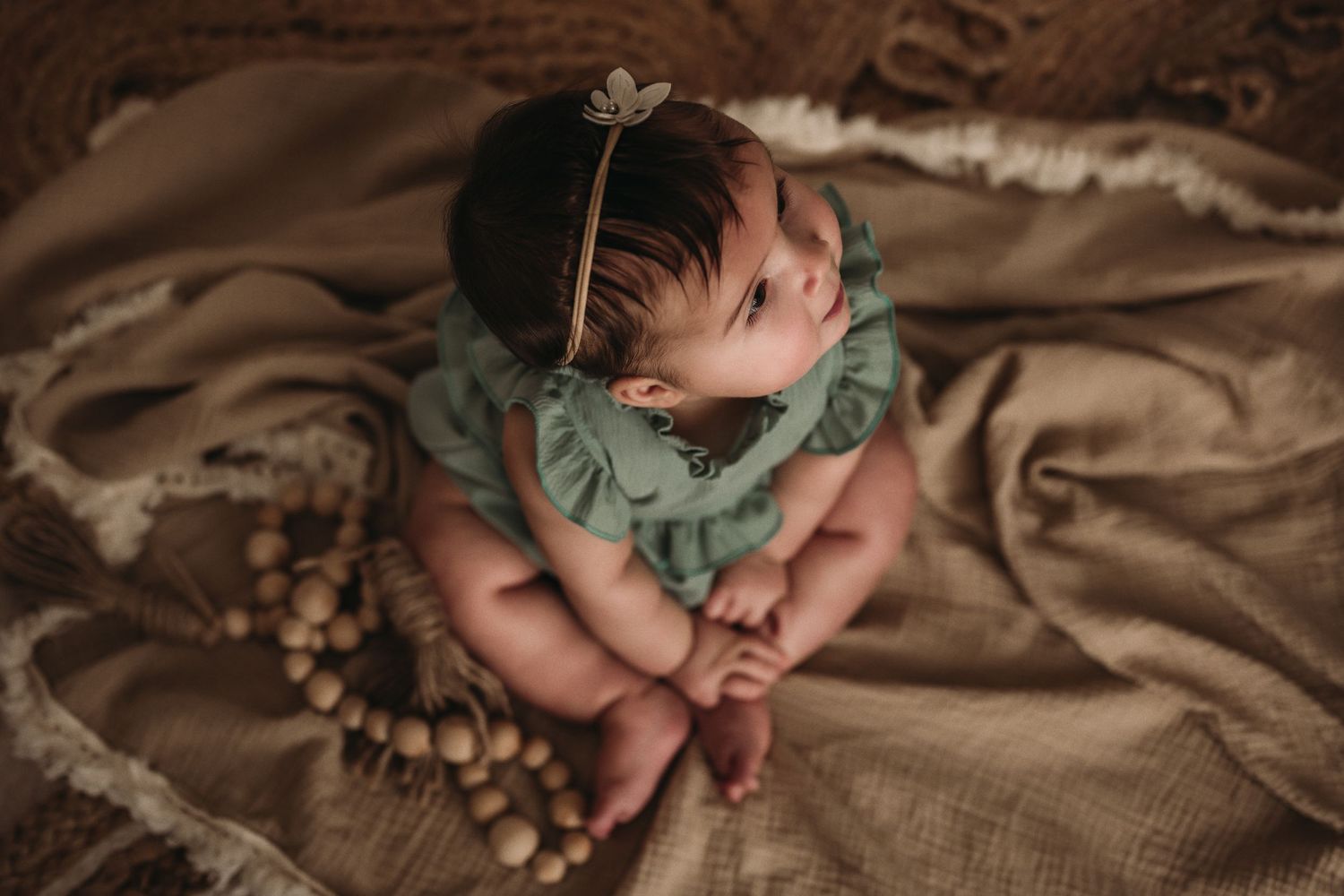 Overhead view of child in mint green ruffled outfit on textured brown blanket.
