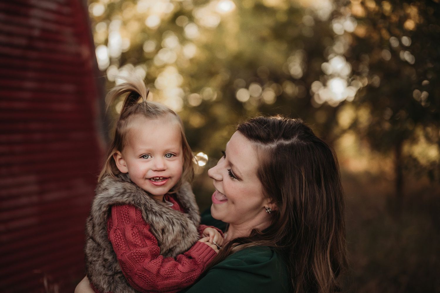 Candid moment of joy shared between parent and child by rustic red barn.
