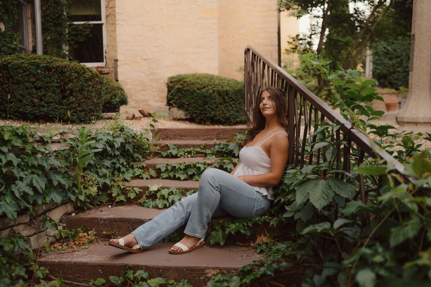 A person relaxes on outdoor stone steps with ivy climbing along the railing.