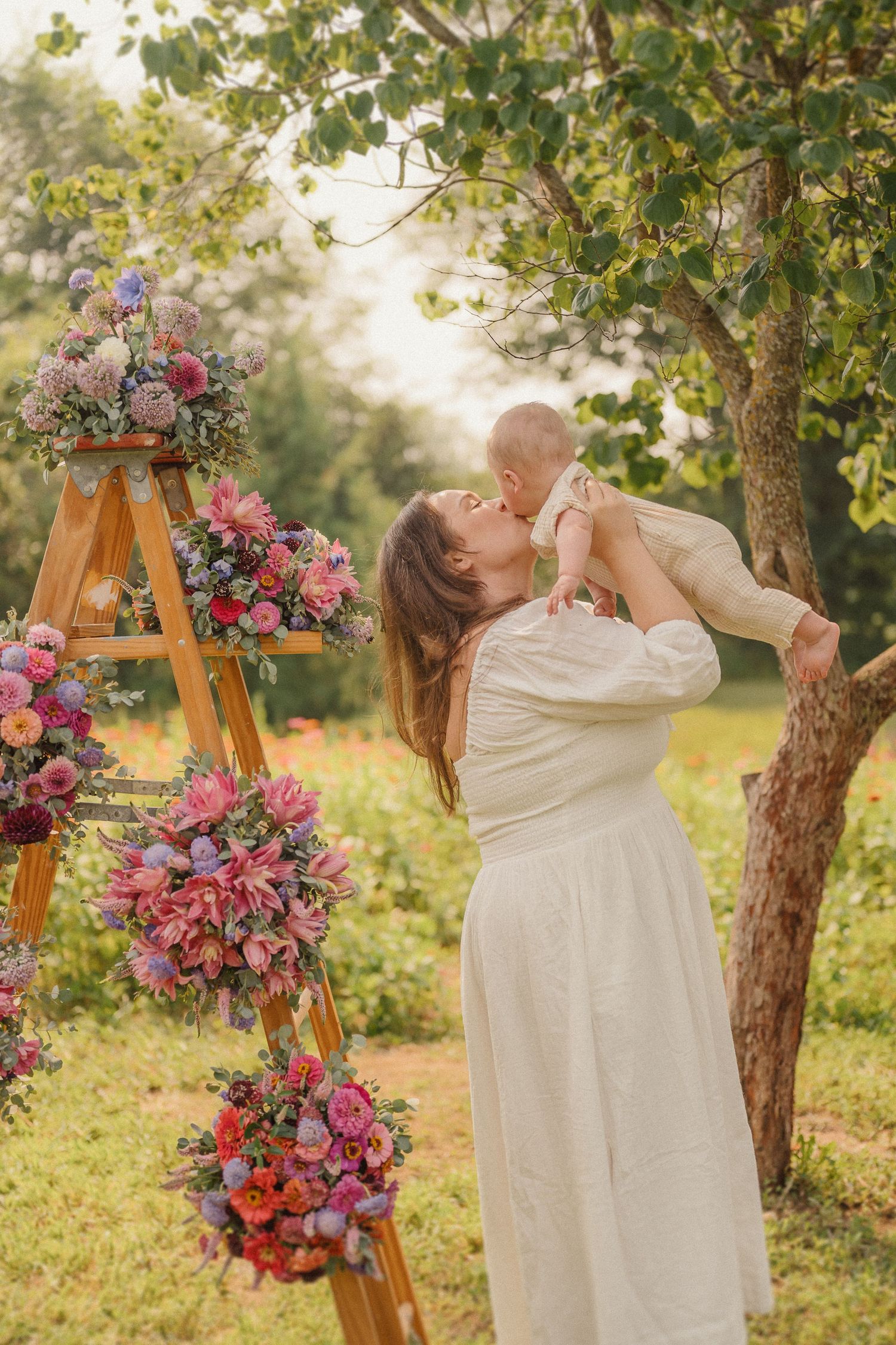 Dreamy outdoor portrait with a wooden ladder decorated in vibrant pink and purple flowers at sunset.