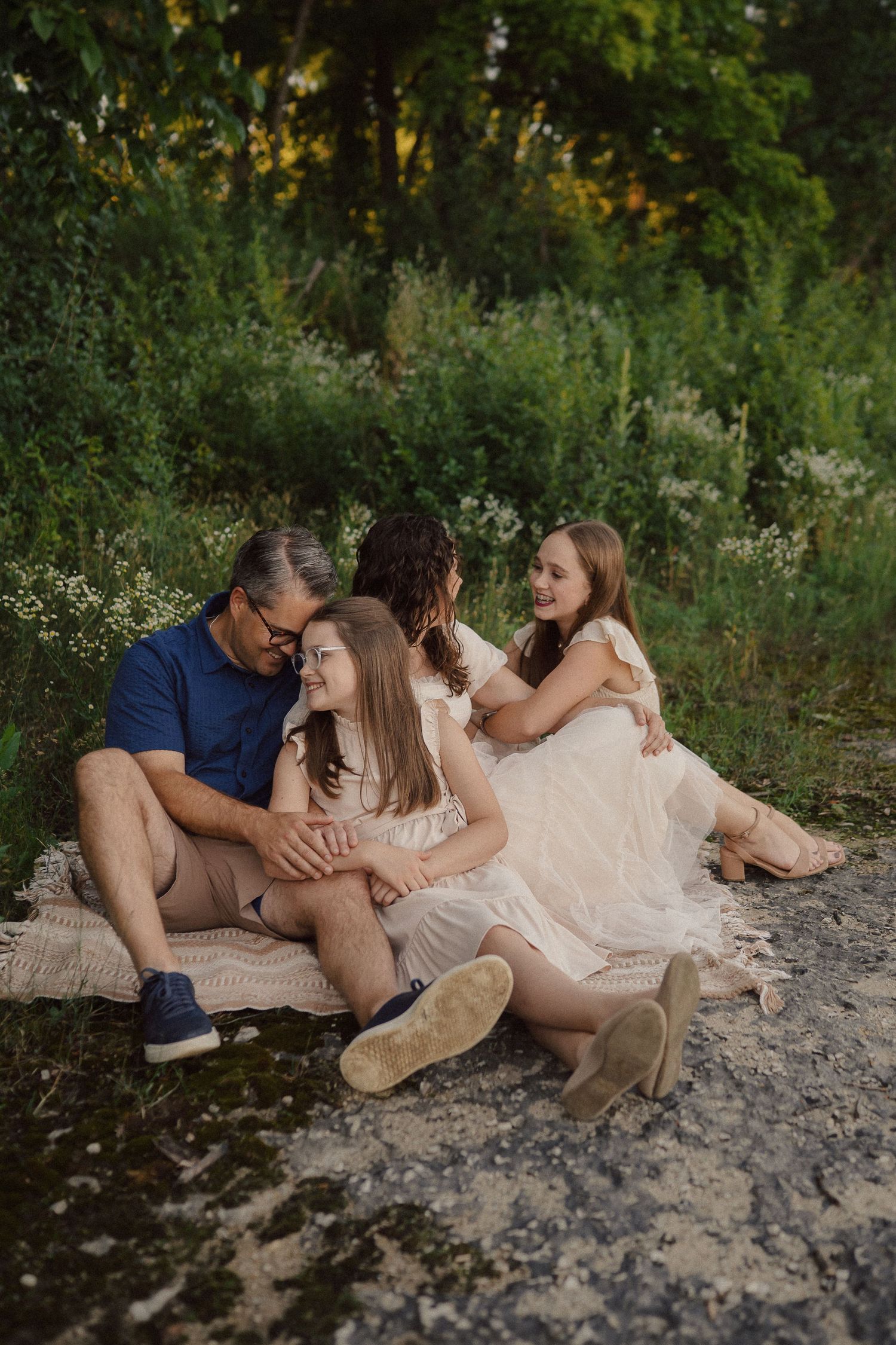 A family sits together on a blanket during a golden hour photoshoot in a natural outdoor setting.