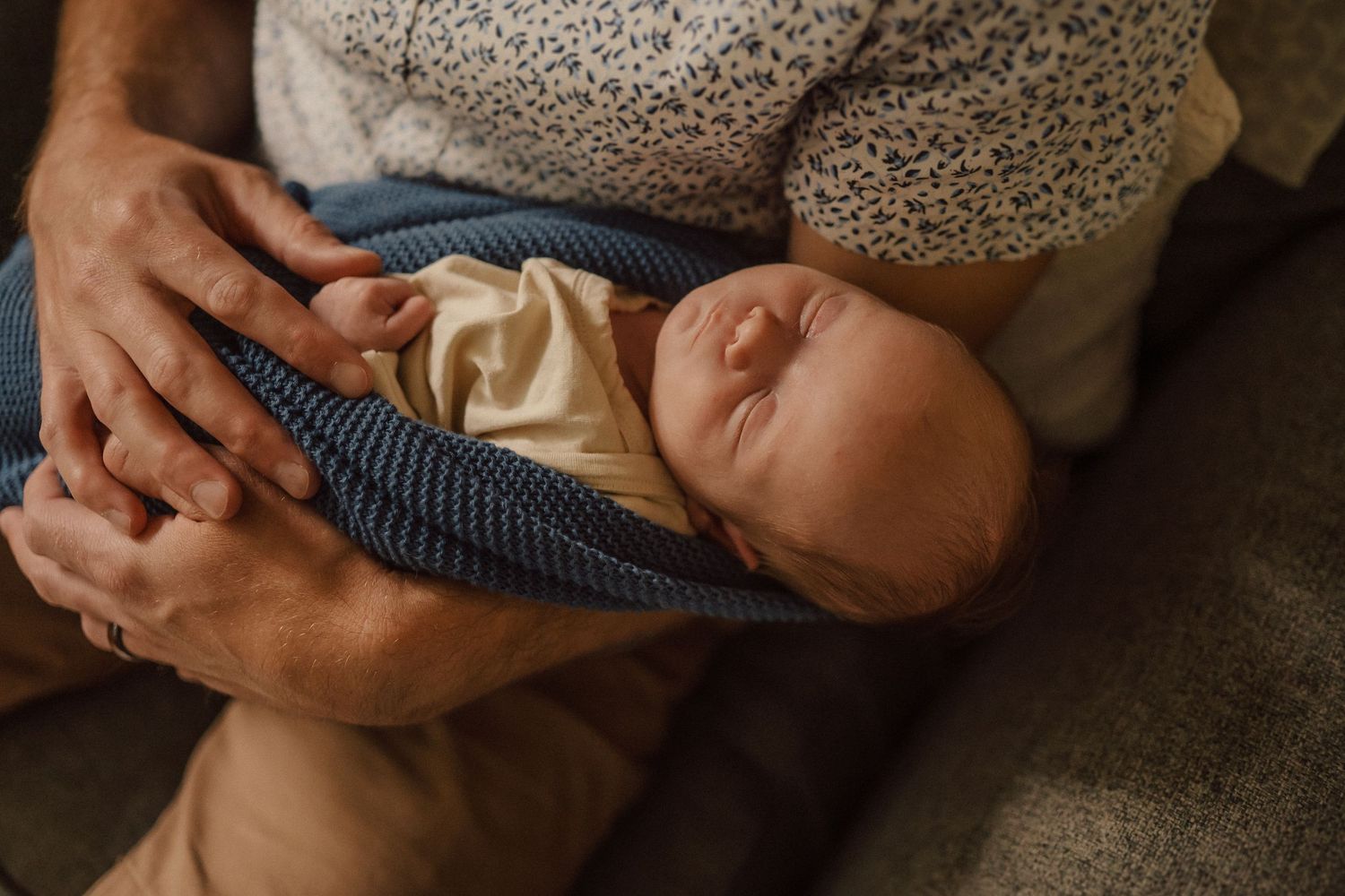 A sleeping infant wrapped in cream and blue textiles held in caring arms.