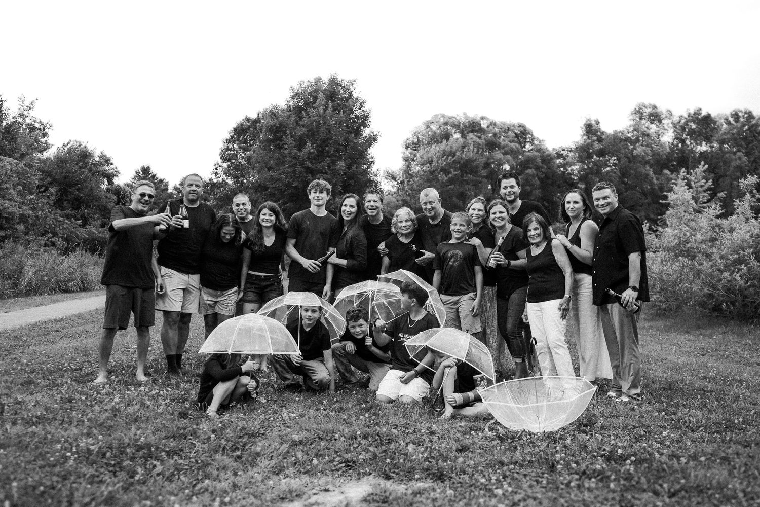 Group photo of extended family posing casually in open field during cloudy day.