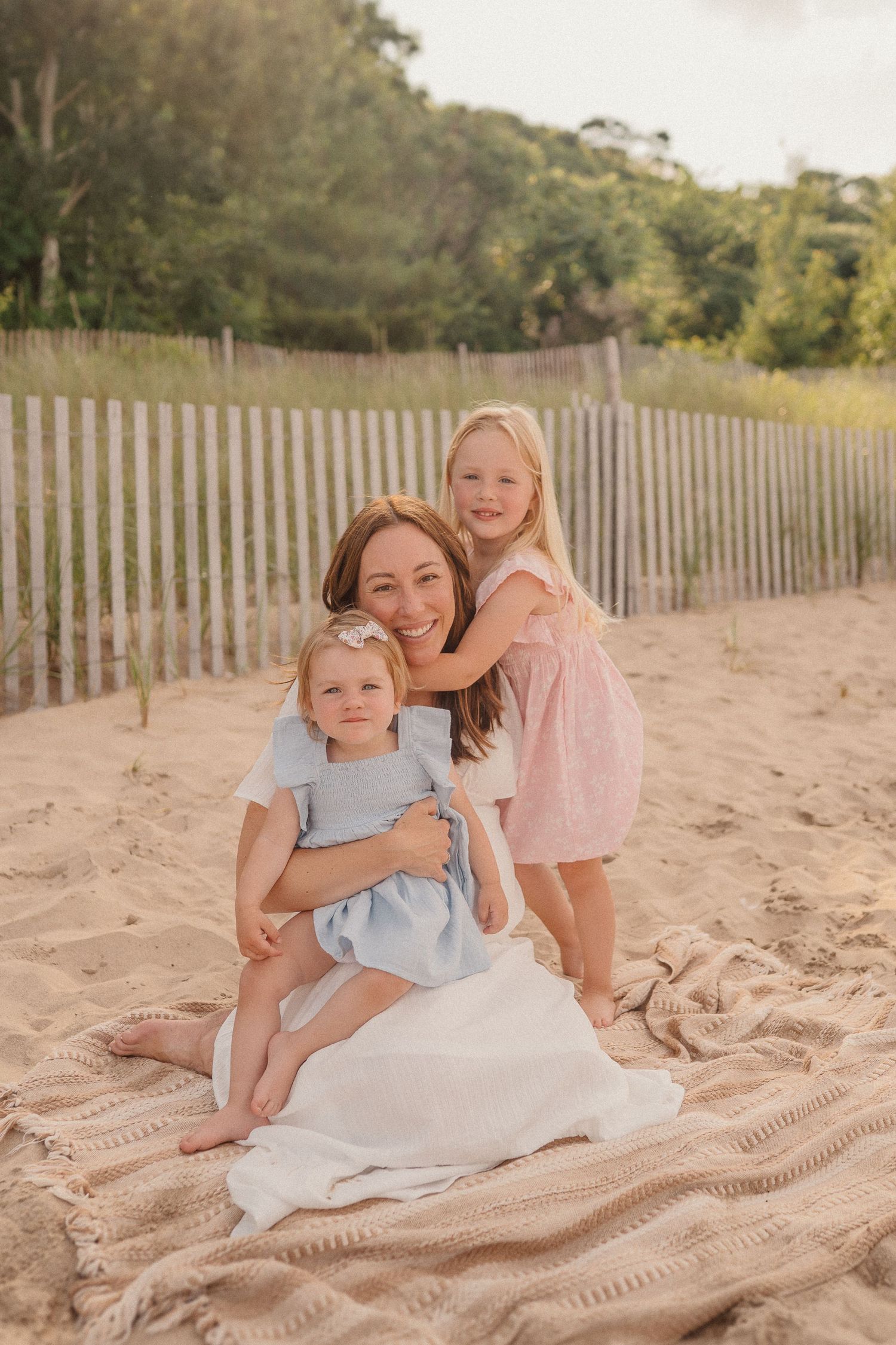 Sweet family beach portrait on a blanket with sand dunes and fence in the background.