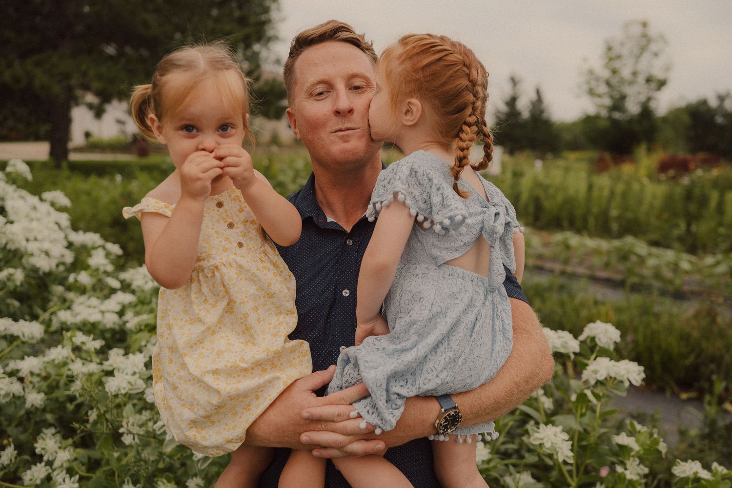 A family playfully interacts together in a lush garden setting during a summer outdoor photoshoot.