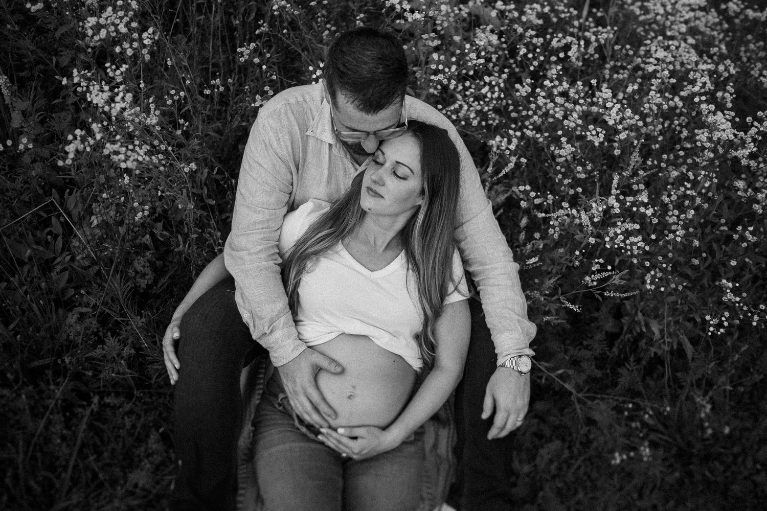 An expecting couple shares an intimate black and white moment outdoors while cradling the baby bump.