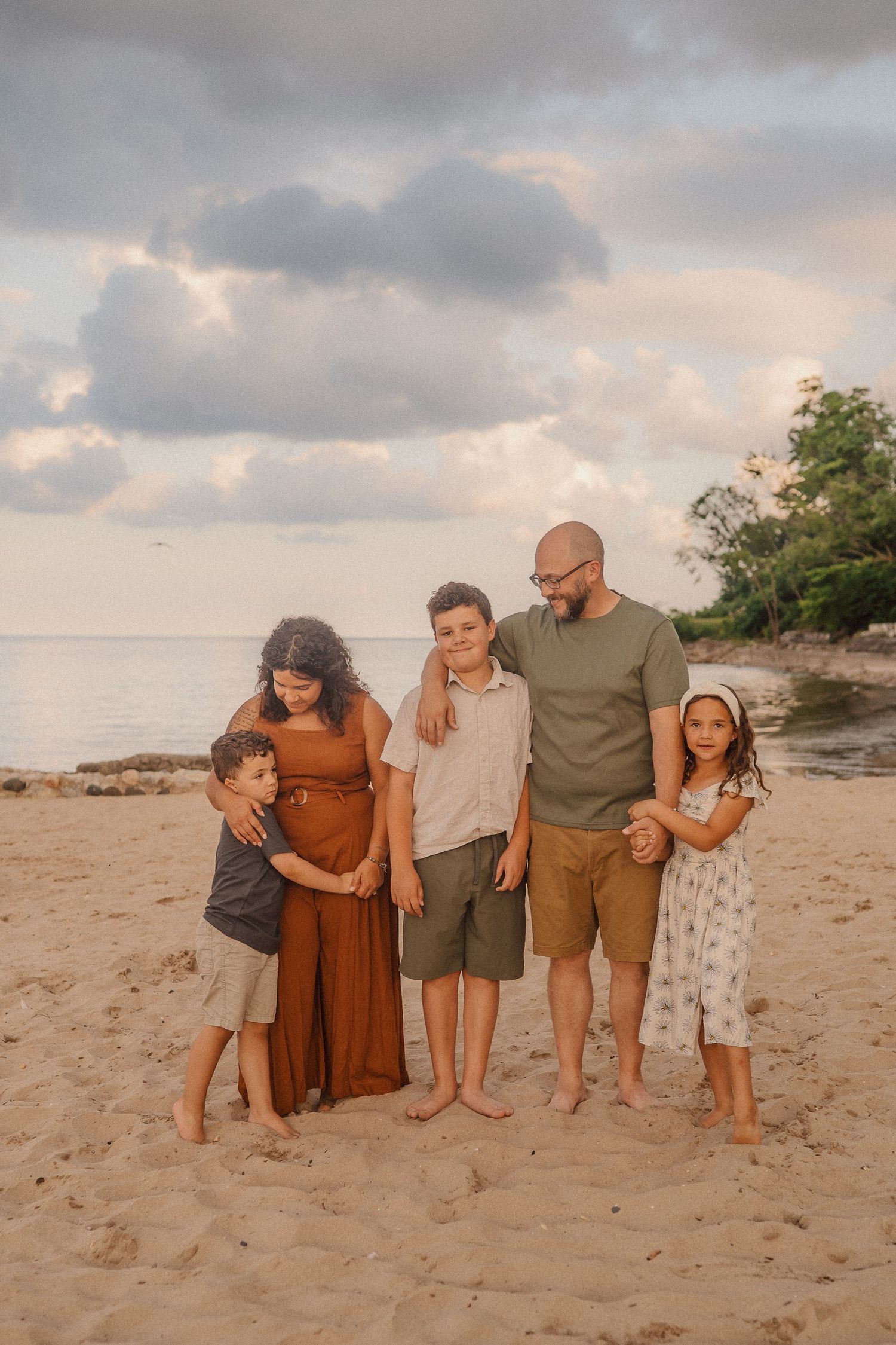 A family group poses together on a sandy beach at sunset with cloudy skies in the background.