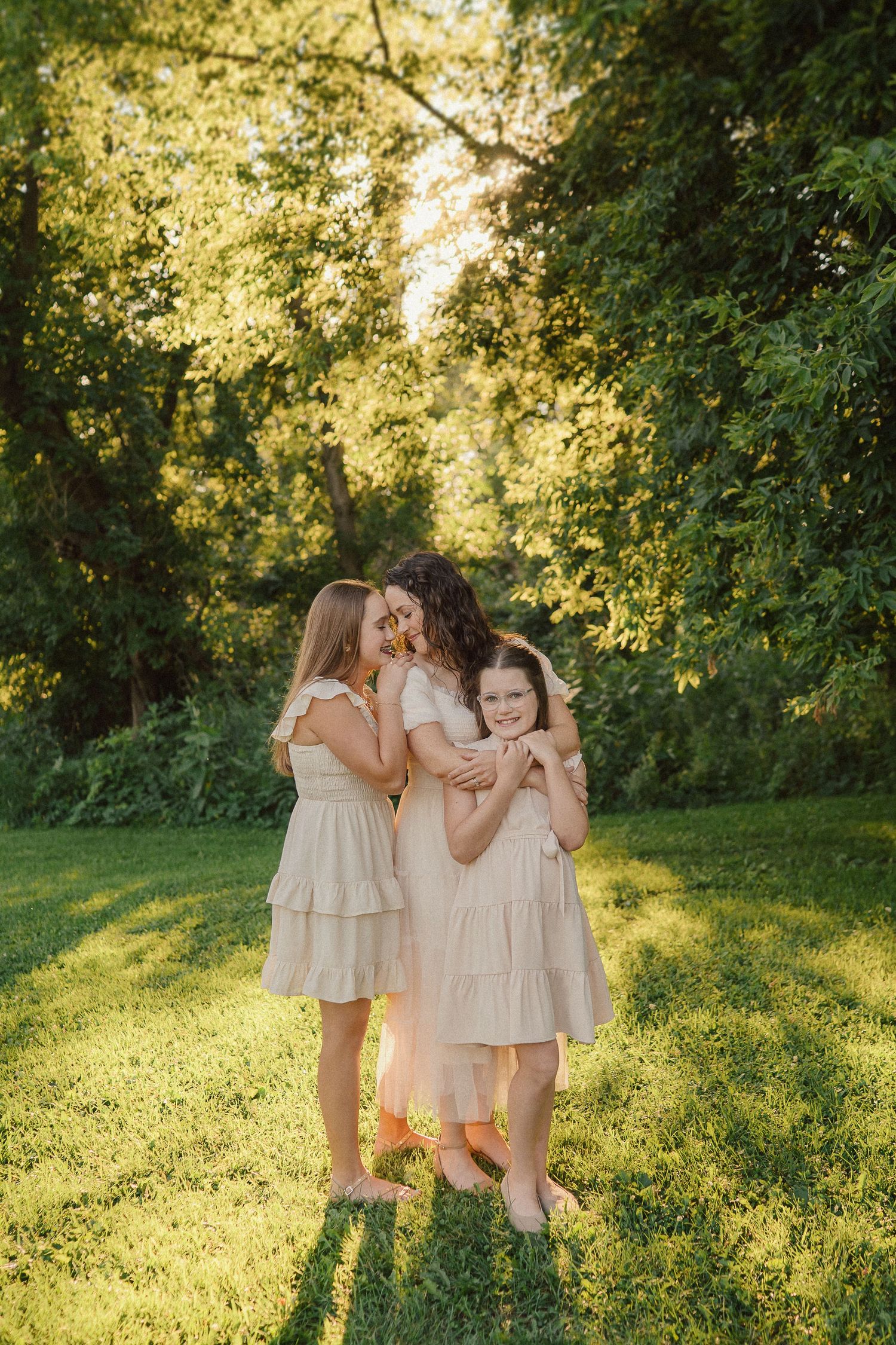 A joyful family embraces in a sun-drenched meadow wearing coordinated beige dresses during golden hour.