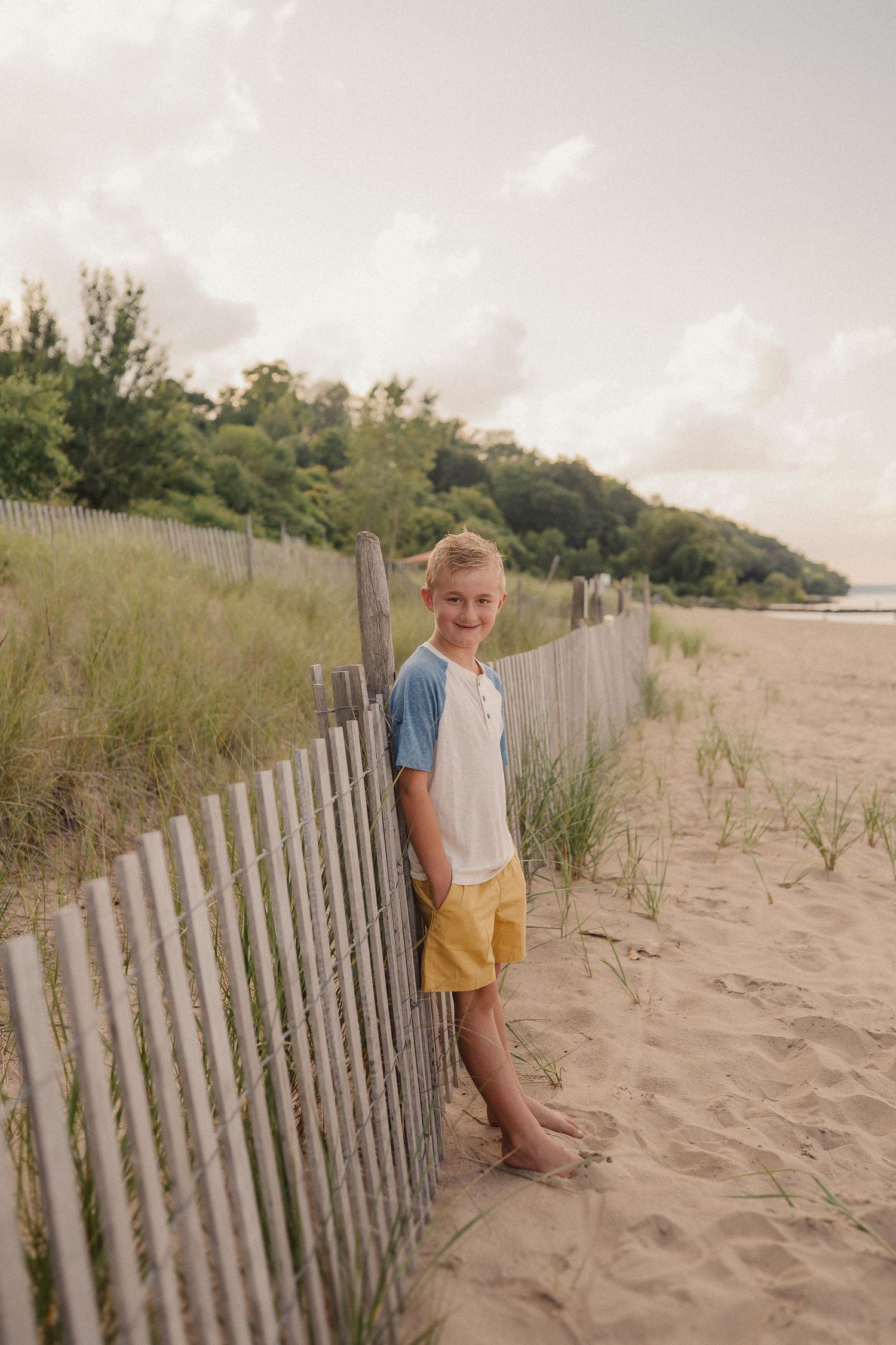 A sandy beach pathway lined with wooden fences leads through coastal dunes at sunset.