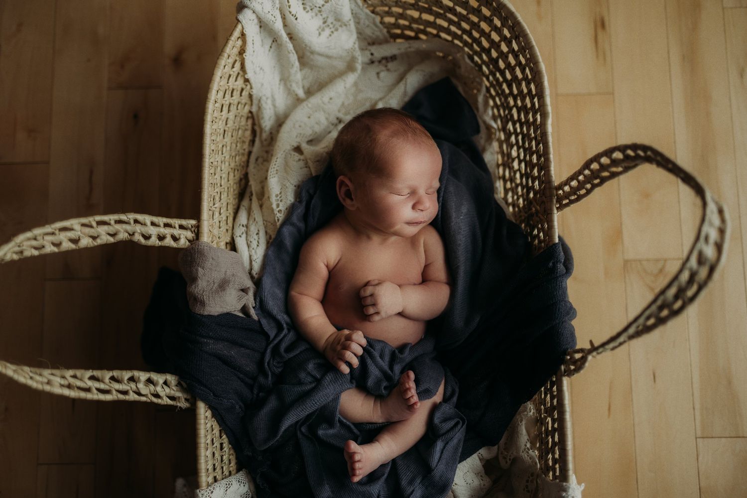 Sleeping newborn rests peacefully in a woven bassinet with dark and light fabrics.