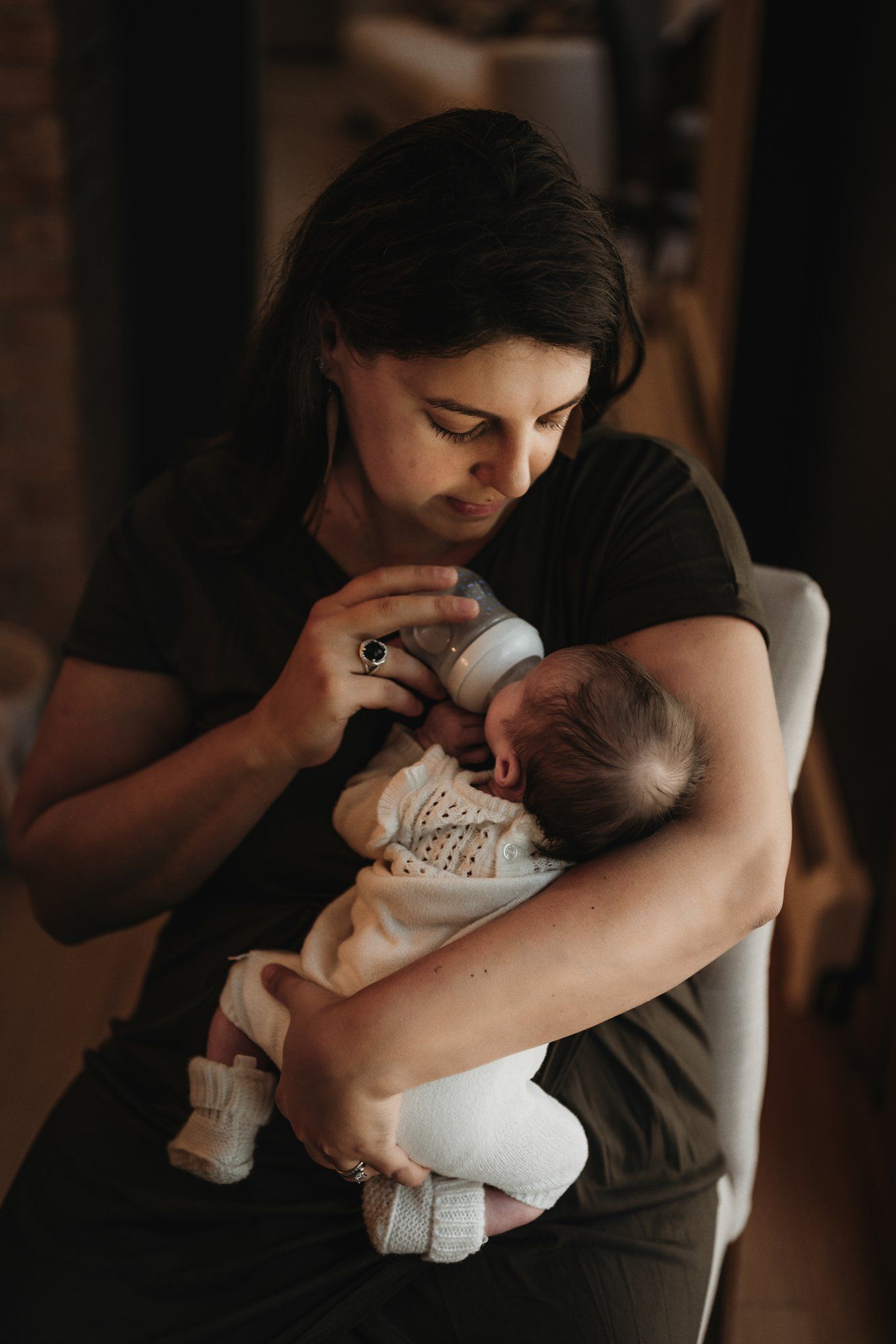 Intimate portrait of a parent cradling and gazing at their newborn baby in dim lighting.