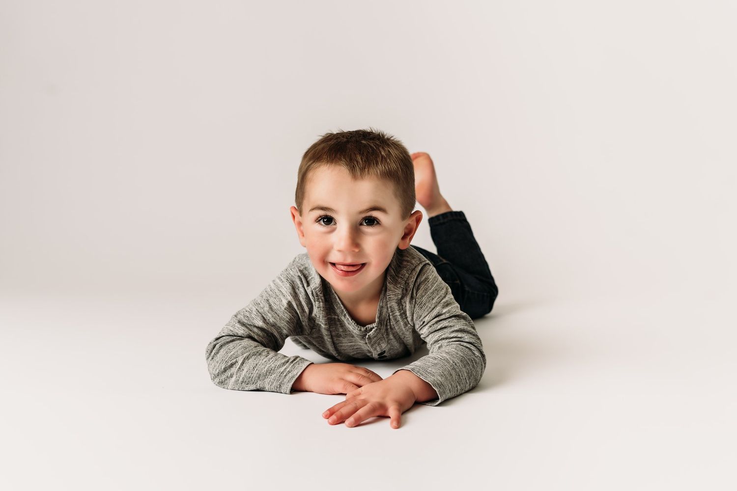 Playful pose lying on stomach on white background wearing gray sweater.