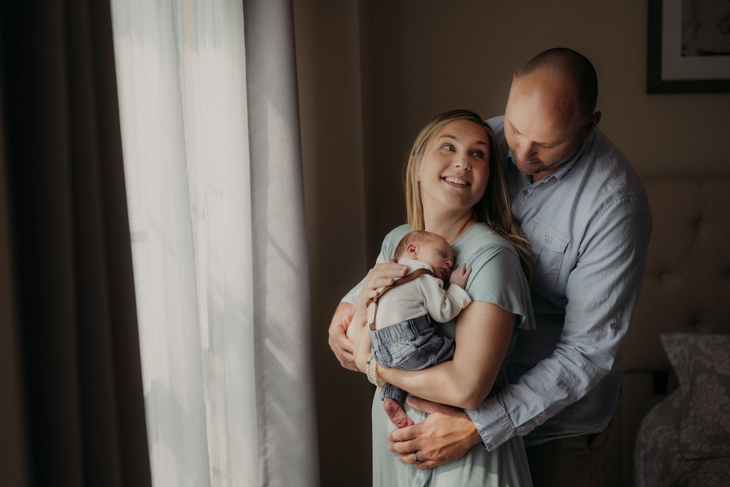 Intimate family portrait by window with natural lighting and soft expressions.
