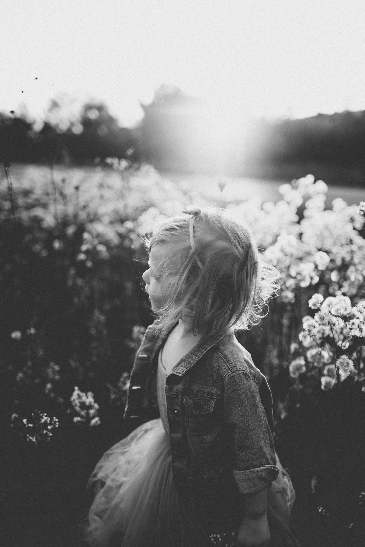 Black and white portrait of child in denim jacket surrounded by wildflowers.