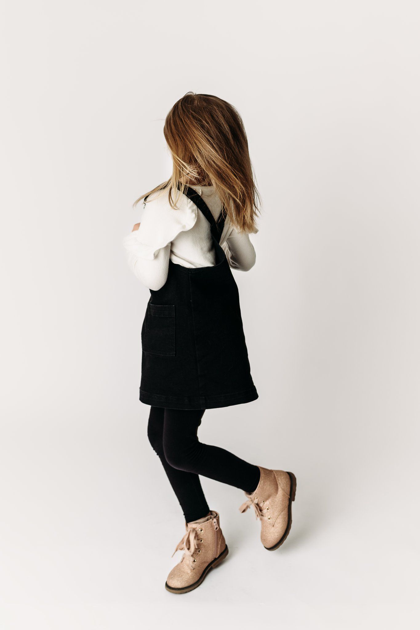 Child in black jumper dress and white top dancing with hair covering face.
