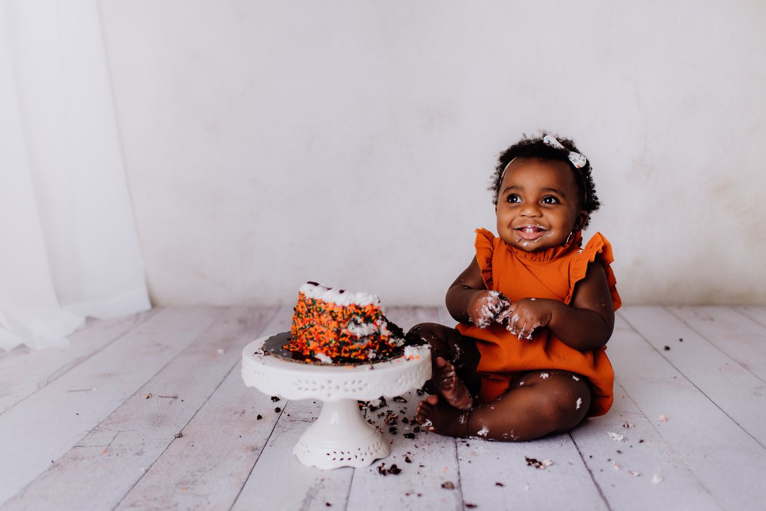 Happy child with cake crumbs during cake smash photography session on white wooden floor.