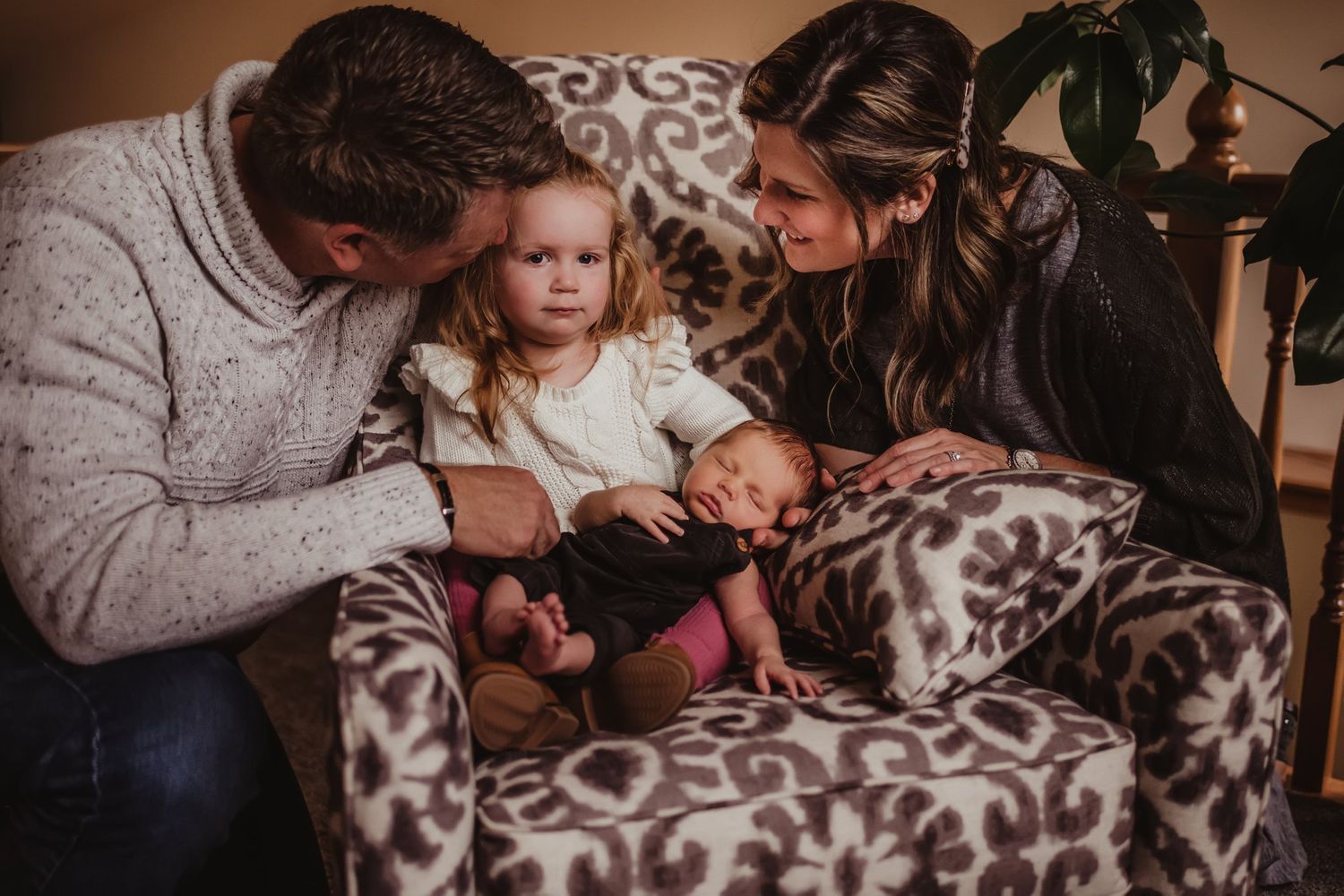 Intimate family portrait on a patterned couch showing tender interaction with a newborn baby.