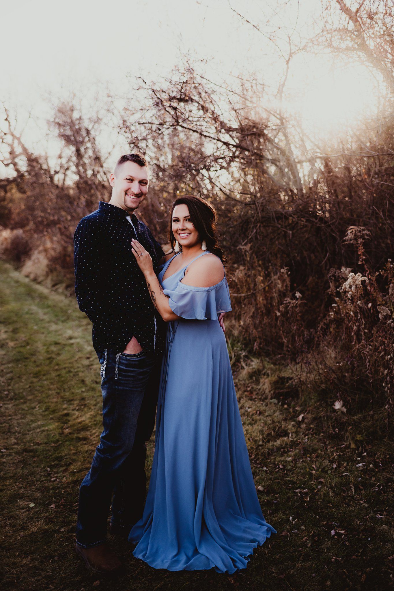 A couple poses together outdoors, with her wearing a flowing blue formal gown.