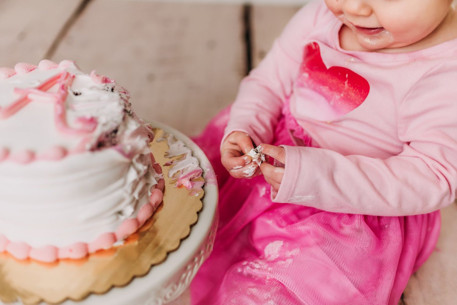 Close-up of hands reaching for pink and white decorated celebration cake.