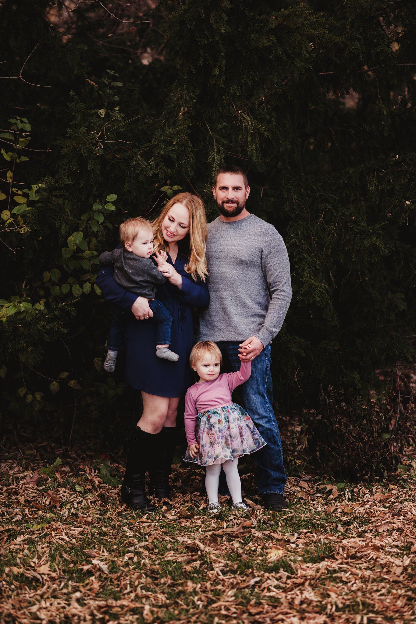 Family of four poses together outdoors on fallen autumn leaves.