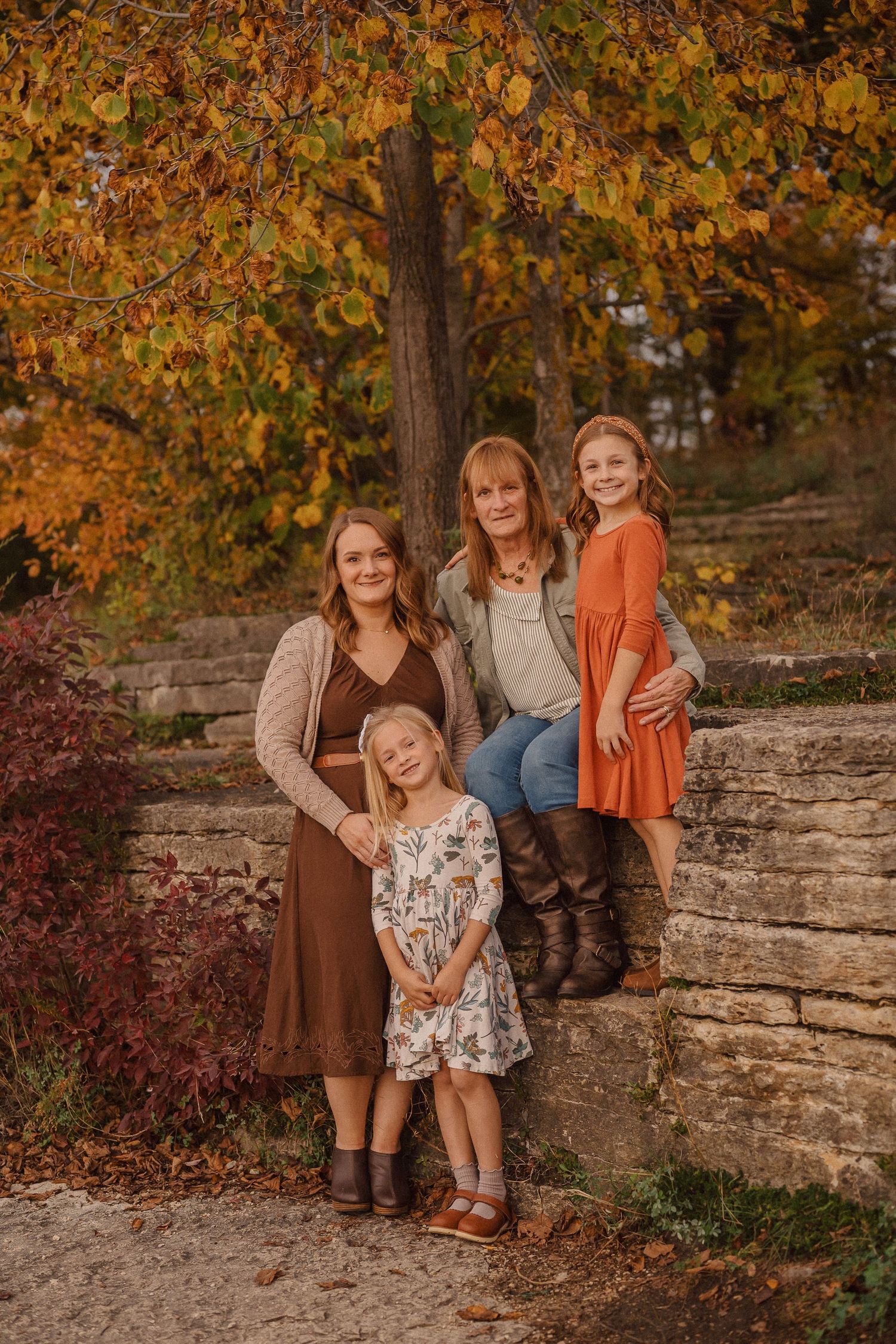 A family sits together on stone steps surrounded by vibrant autumn foliage in warm earth-toned clothing.