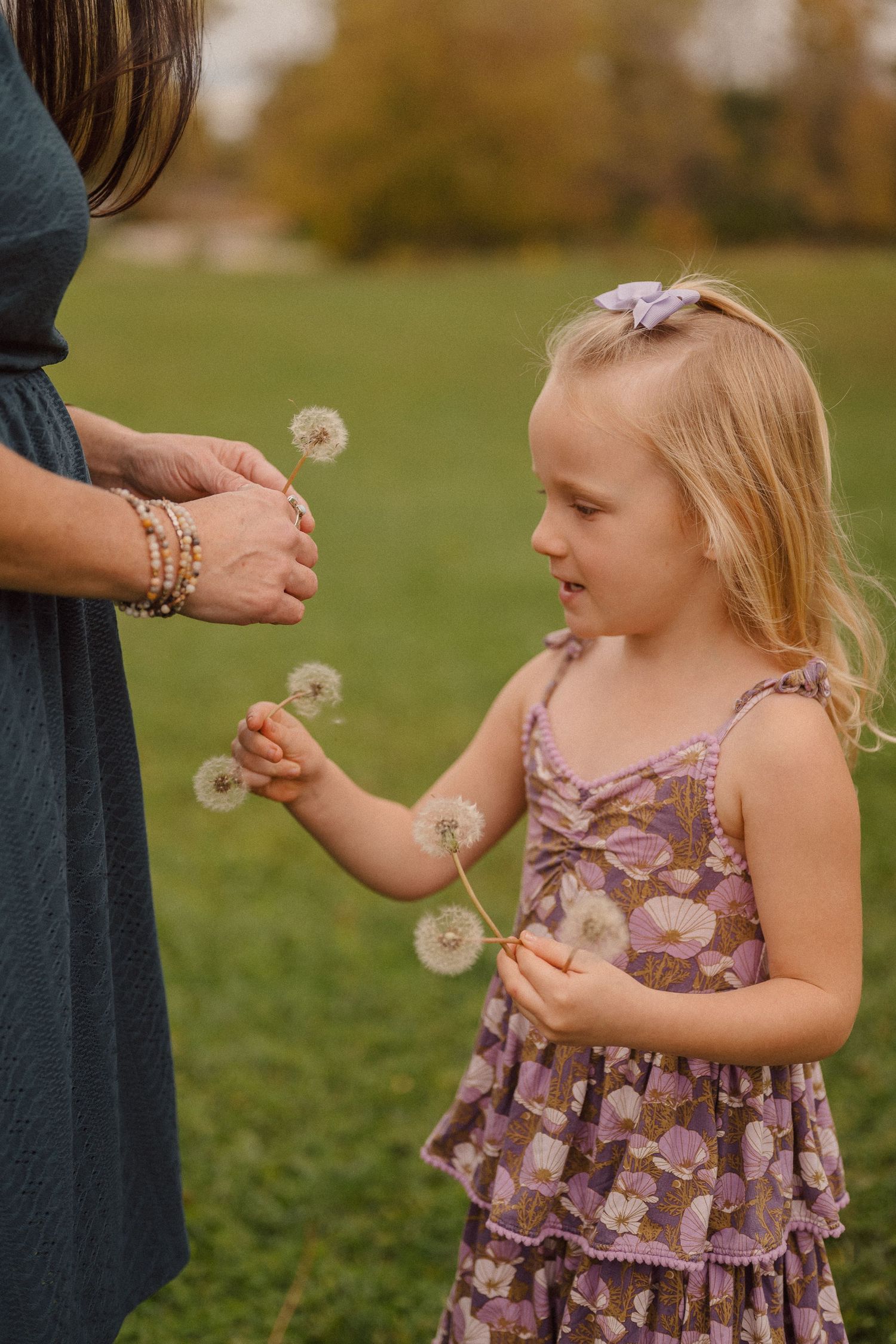 A child in a floral dress discovers the magic of dandelion wishes in a sunlit field.