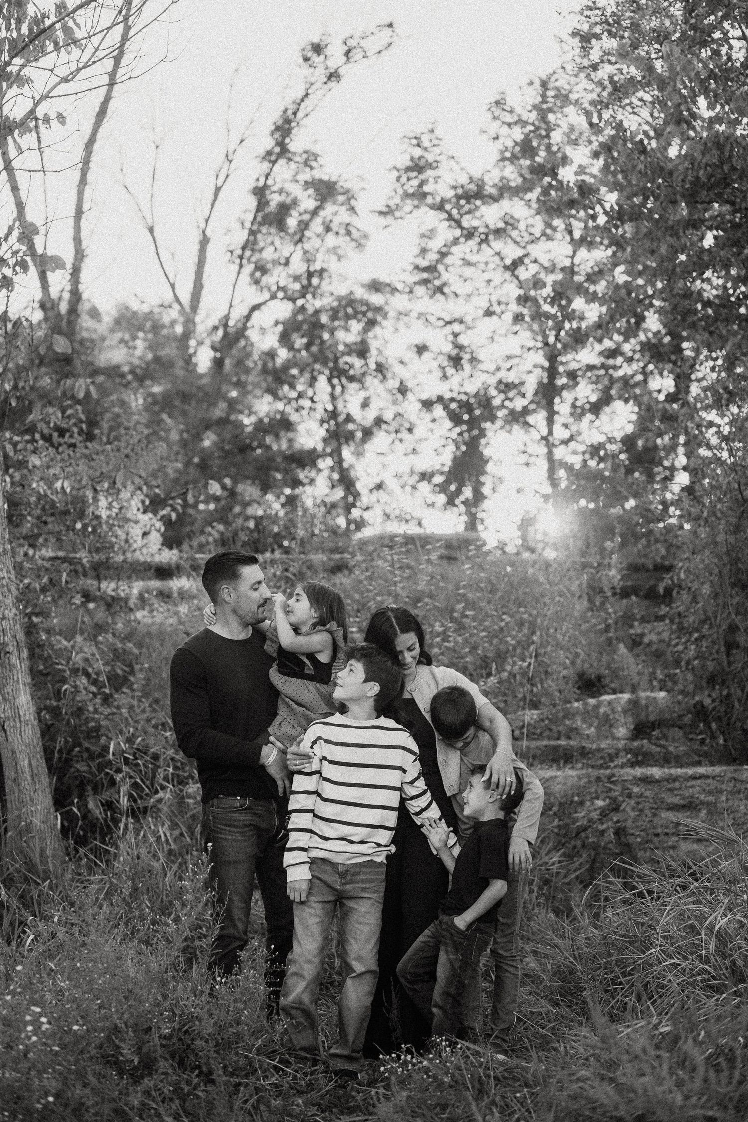 A series of black and white romantic photos showing a couple embracing outdoors among trees and tall grass.
