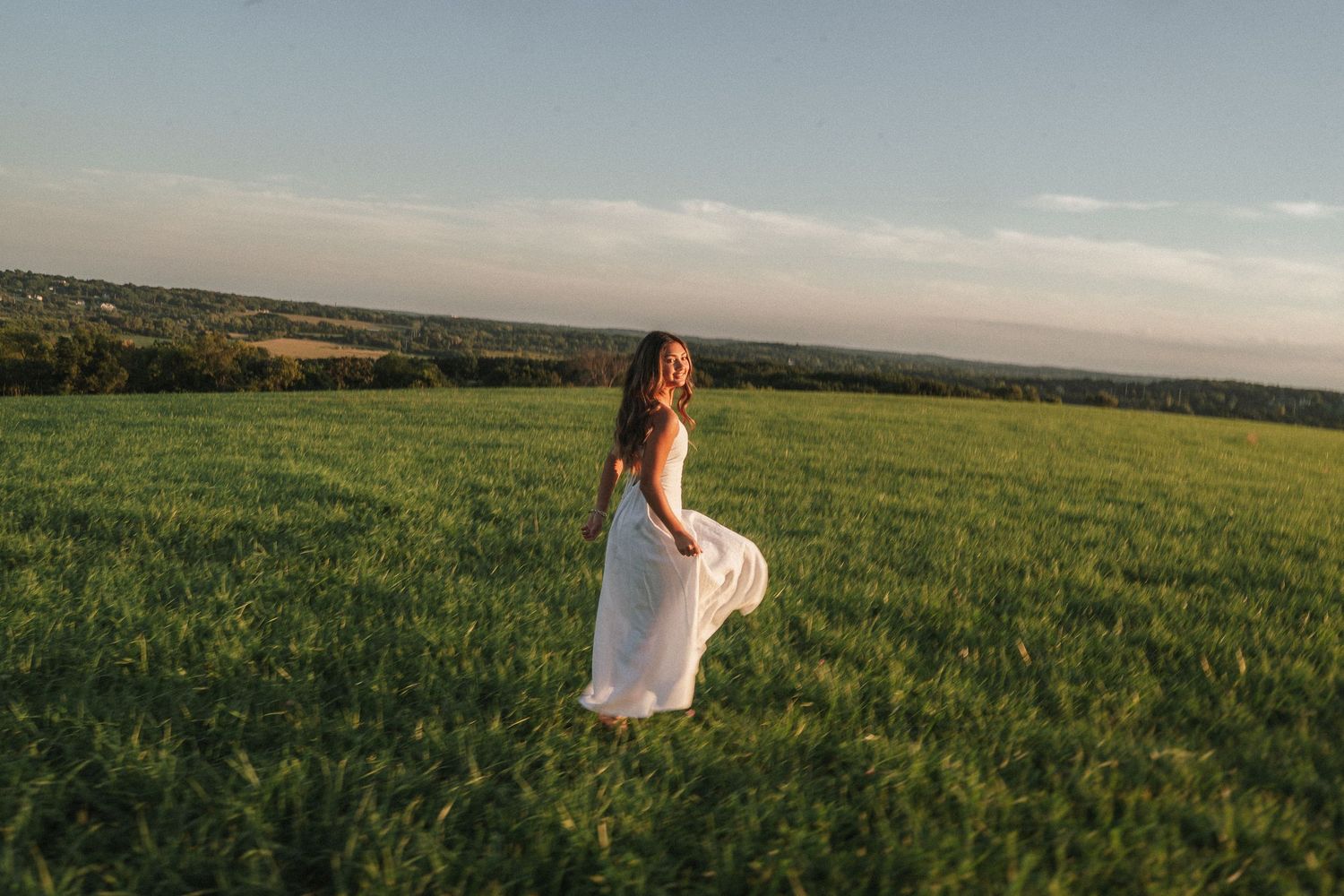 Woman in a dress dancing in a rustic field at dusk.