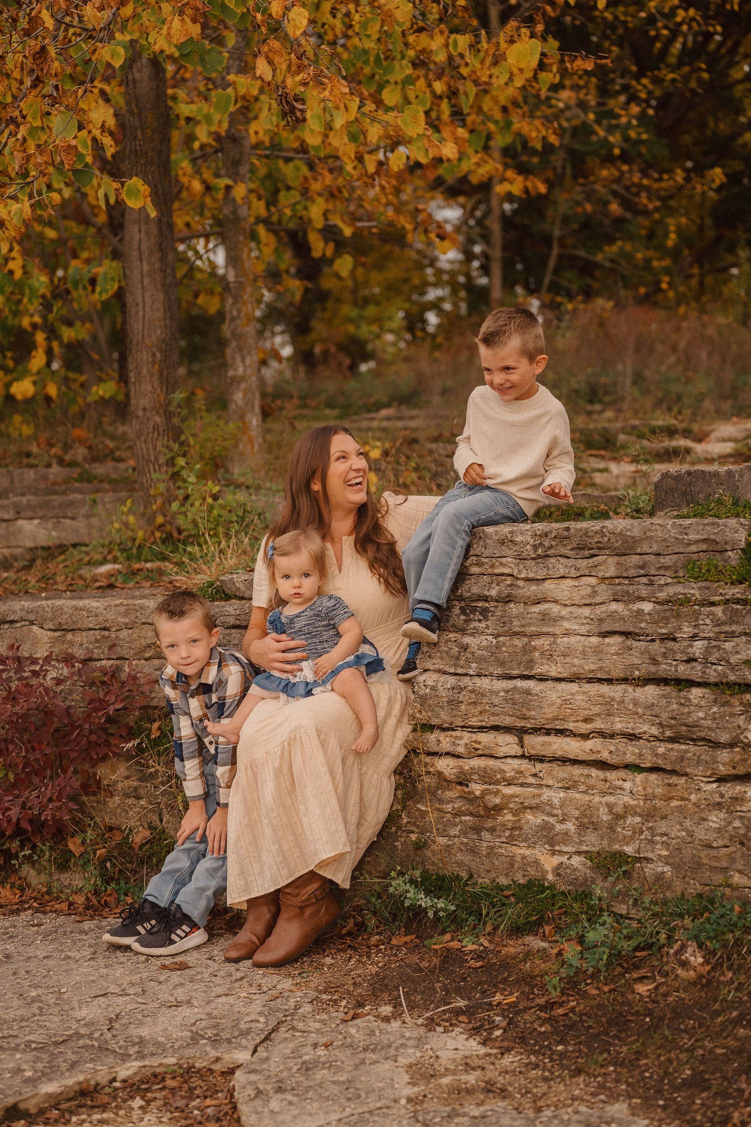 Family relaxing together on stone wall outdoors during autumn photoshoot.