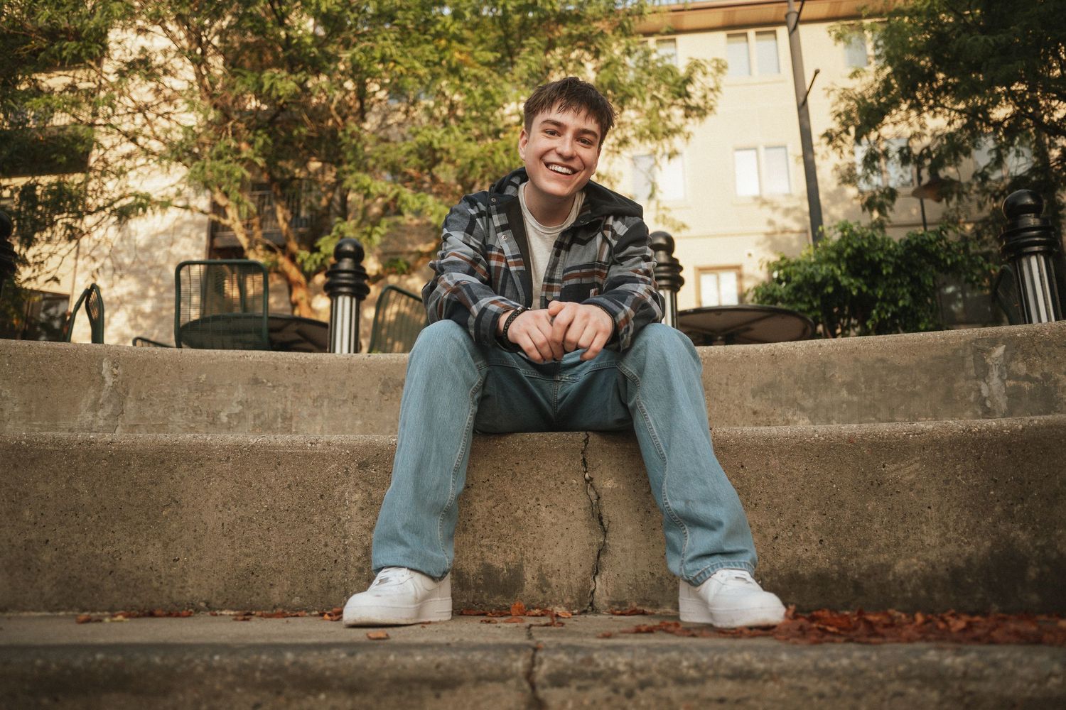 A person in casual clothing sits on a concrete ledge surrounded by autumn leaves and trees.