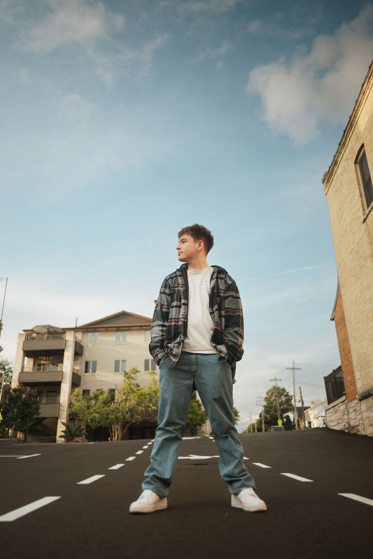Low angle shot of person in denim and white sneakers standing on asphalt parking lot.