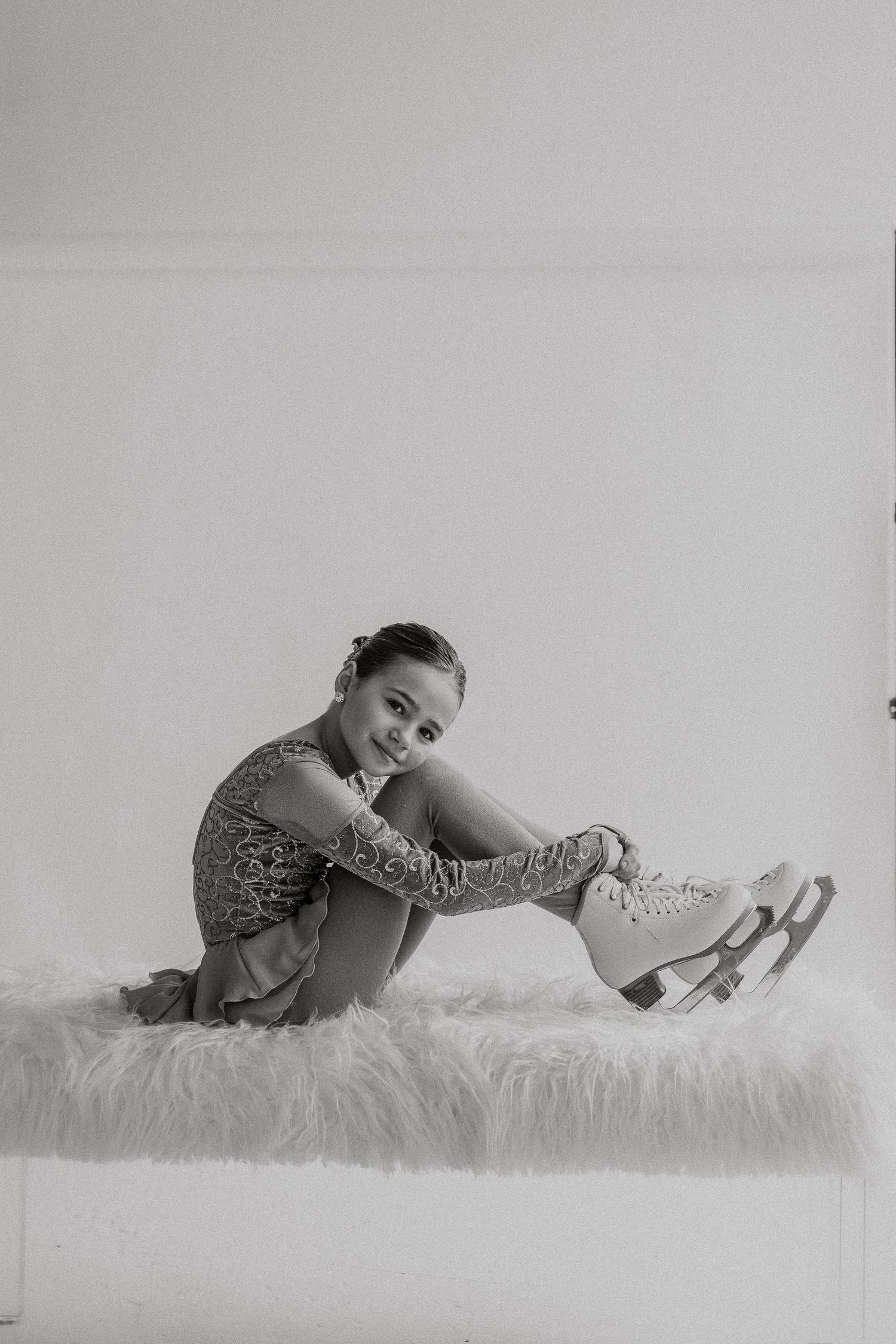 Ice skater in sparkly costume poses on furry surface in black and white studio portrait.