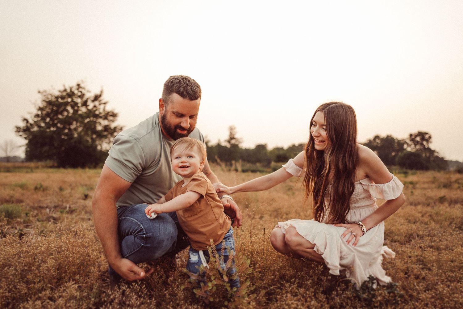 Warm sunset photo of a family sharing a playful moment in a rustic field setting.