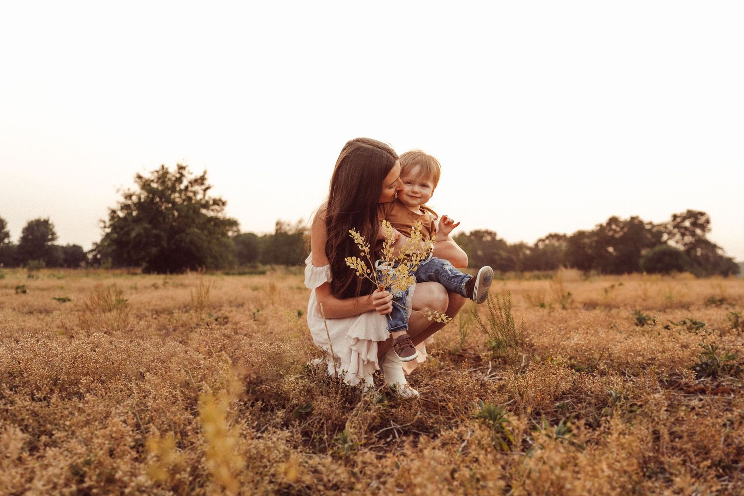 Two people share a tender moment with a child in a rustic field during golden hour.