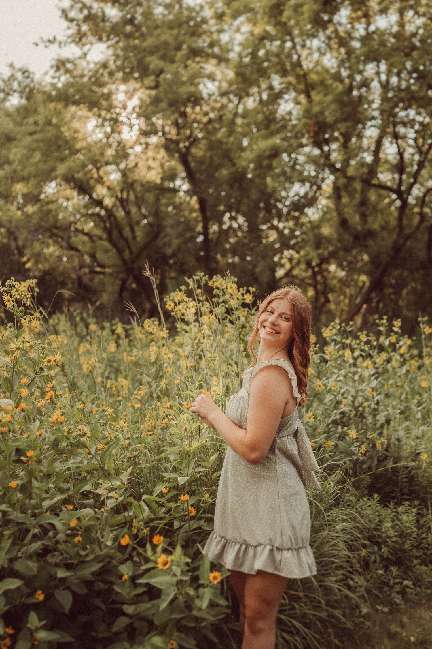 A romantic summer portrait in a garden with yellow wildflowers and a light grey ruffle dress.