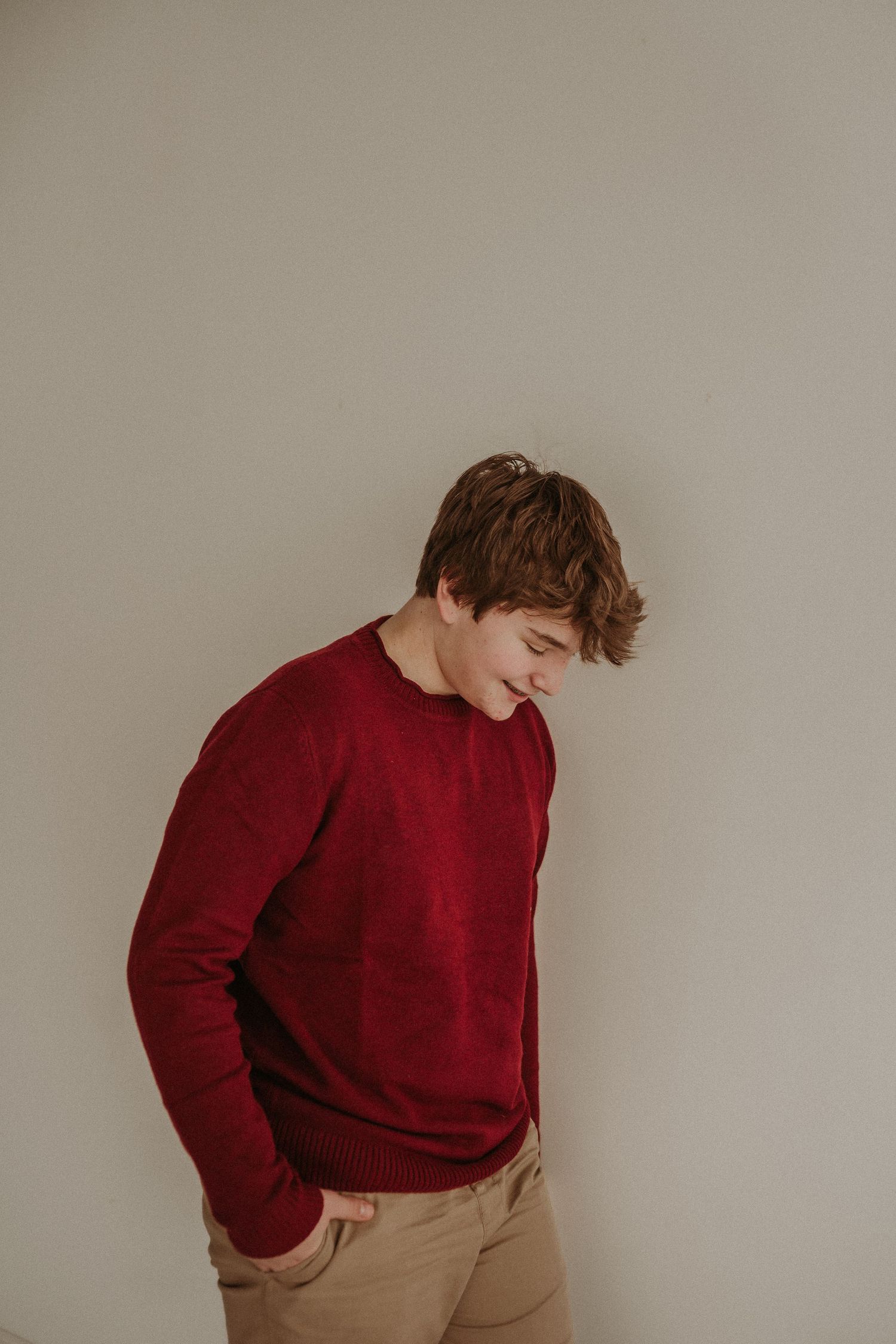 A person in a burgundy sweater and khaki pants poses casually against a neutral wall.