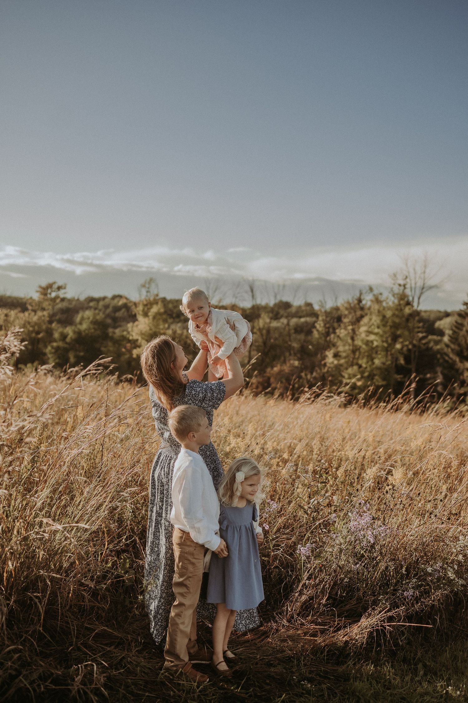 Loving family interaction photographed in golden meadow at sunset.