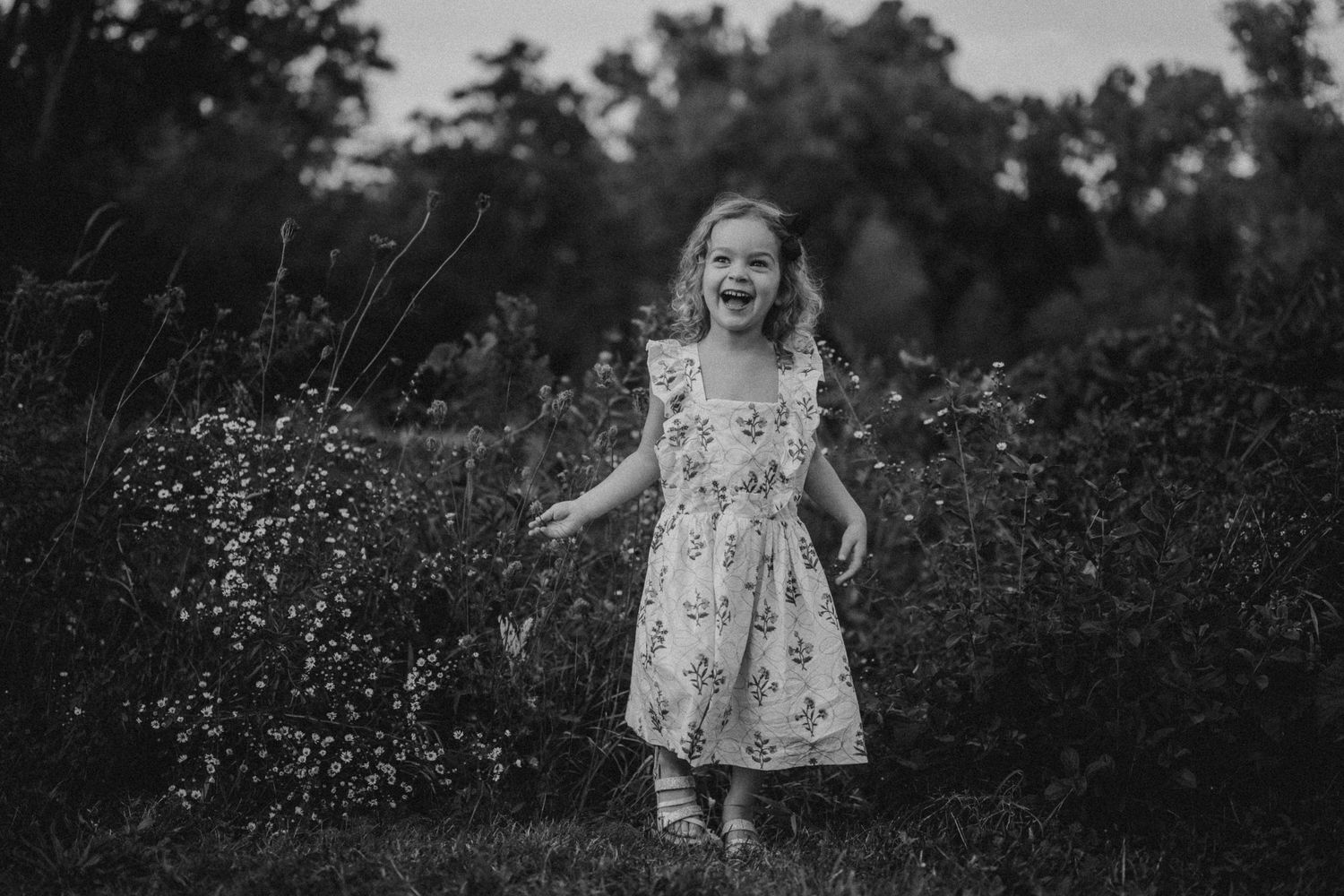 Black and white portrait of a child playing in a field of wildflowers.